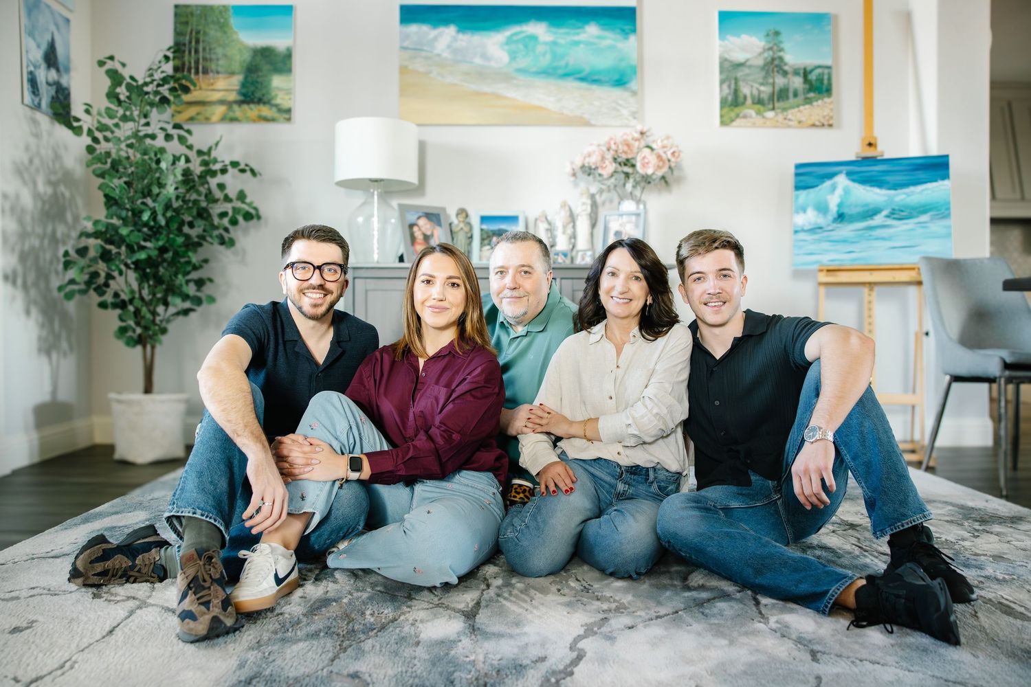 Happy family of five sitting together on a rug in a decorated living room.