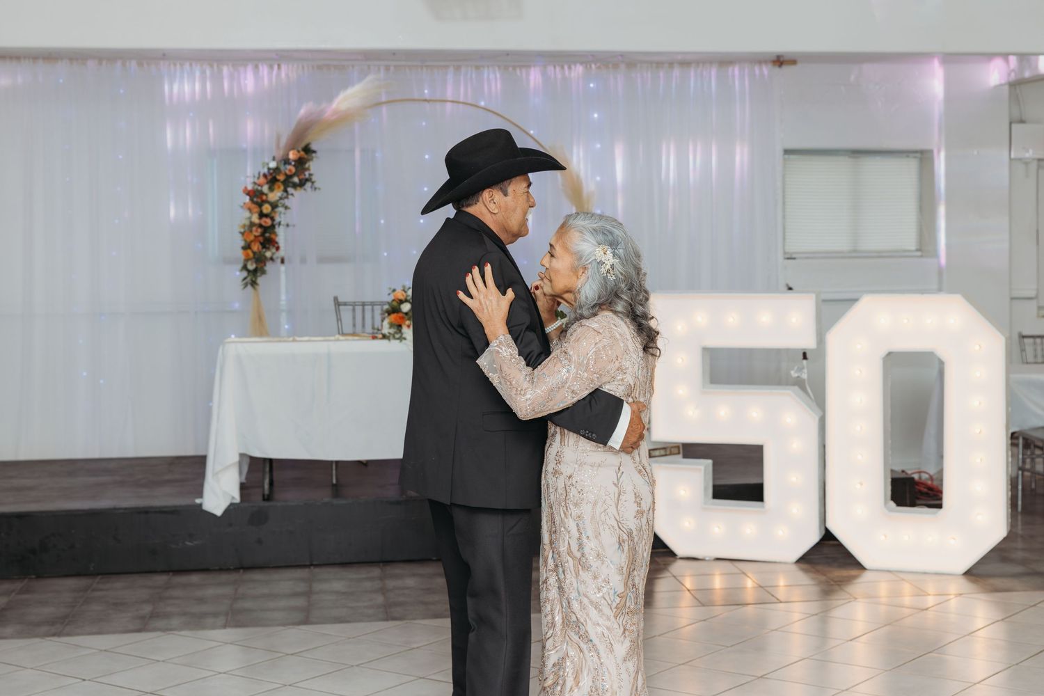 Elderly couple sharing a romantic dance at their 50th wedding anniversary celebration in a decorated banquet hall.