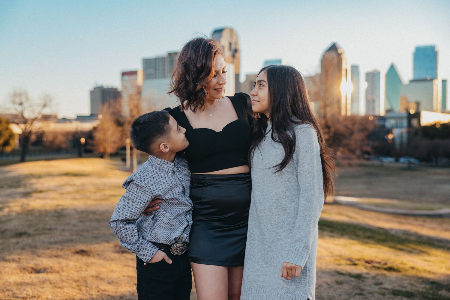 Mother with two children sharing a tender moment outdoors with city skyline in golden hour light.