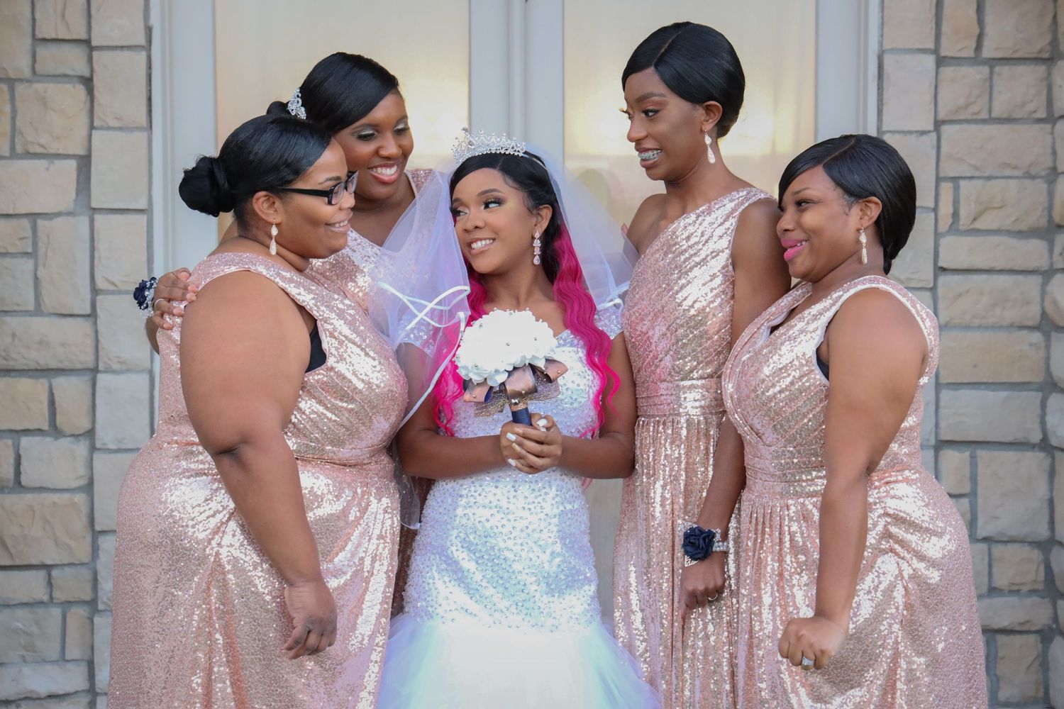 Bride with bridesmaids in rose gold sequin dresses holding white bouquet.
