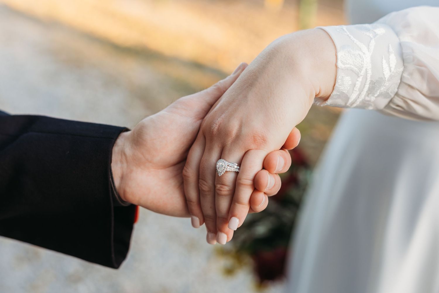 Close-up of a couple holding hands showing a sparkling diamond engagement ring on the bride's finger.