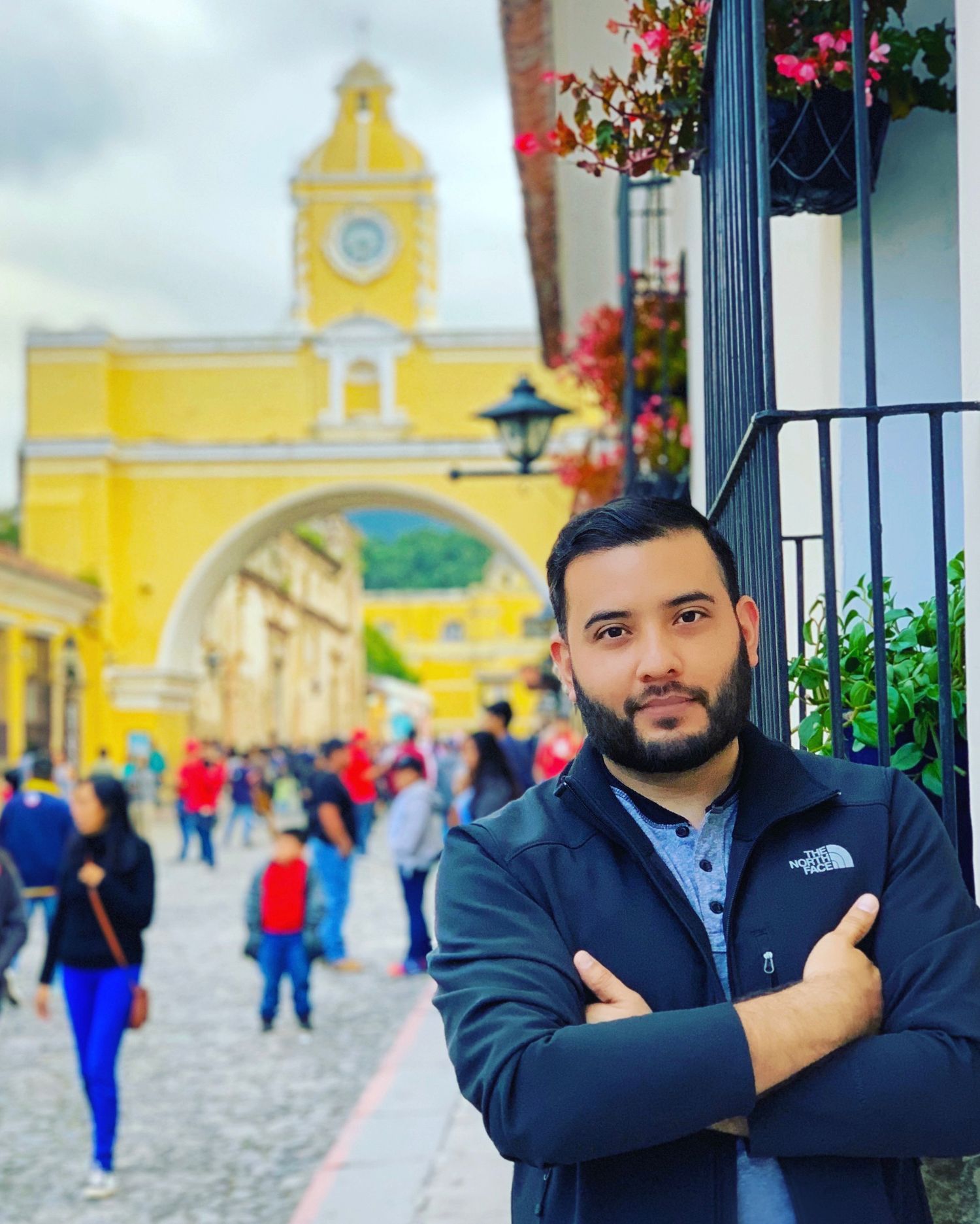 Young bearded man with crossed arms posing in front of the iconic Santa Catalina Arch in Antigua, Guatemala.