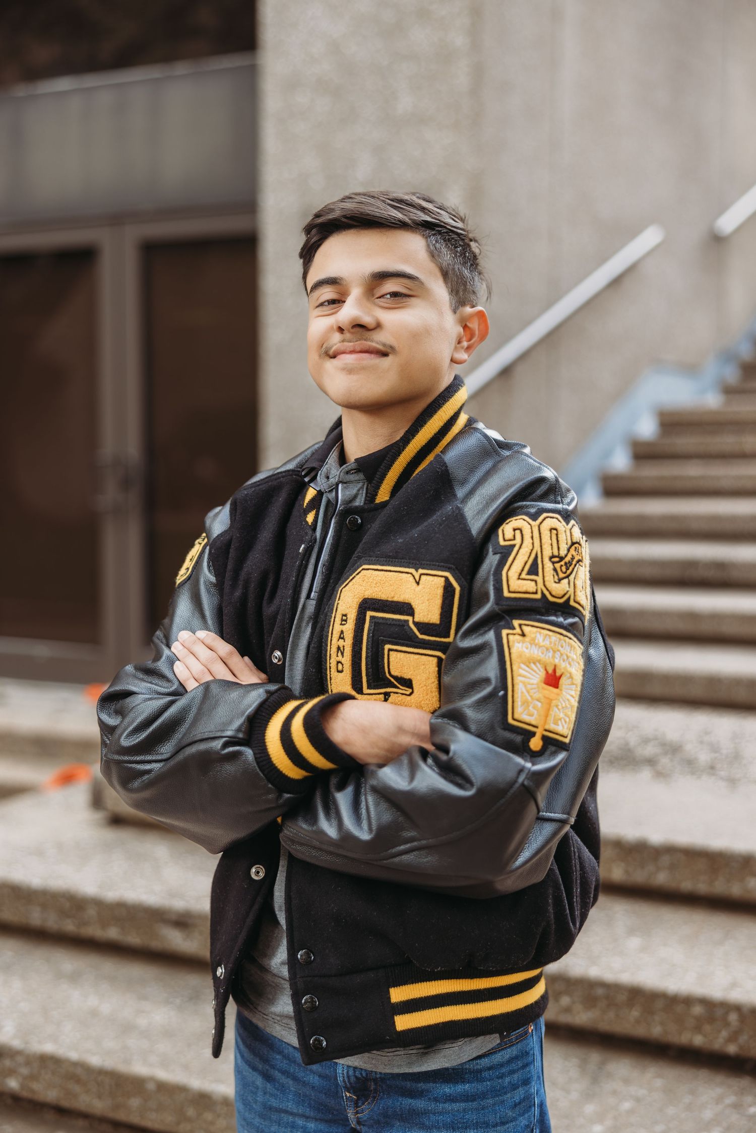 Young man in black and gold varsity jacket posing with arms crossed for senior photos.