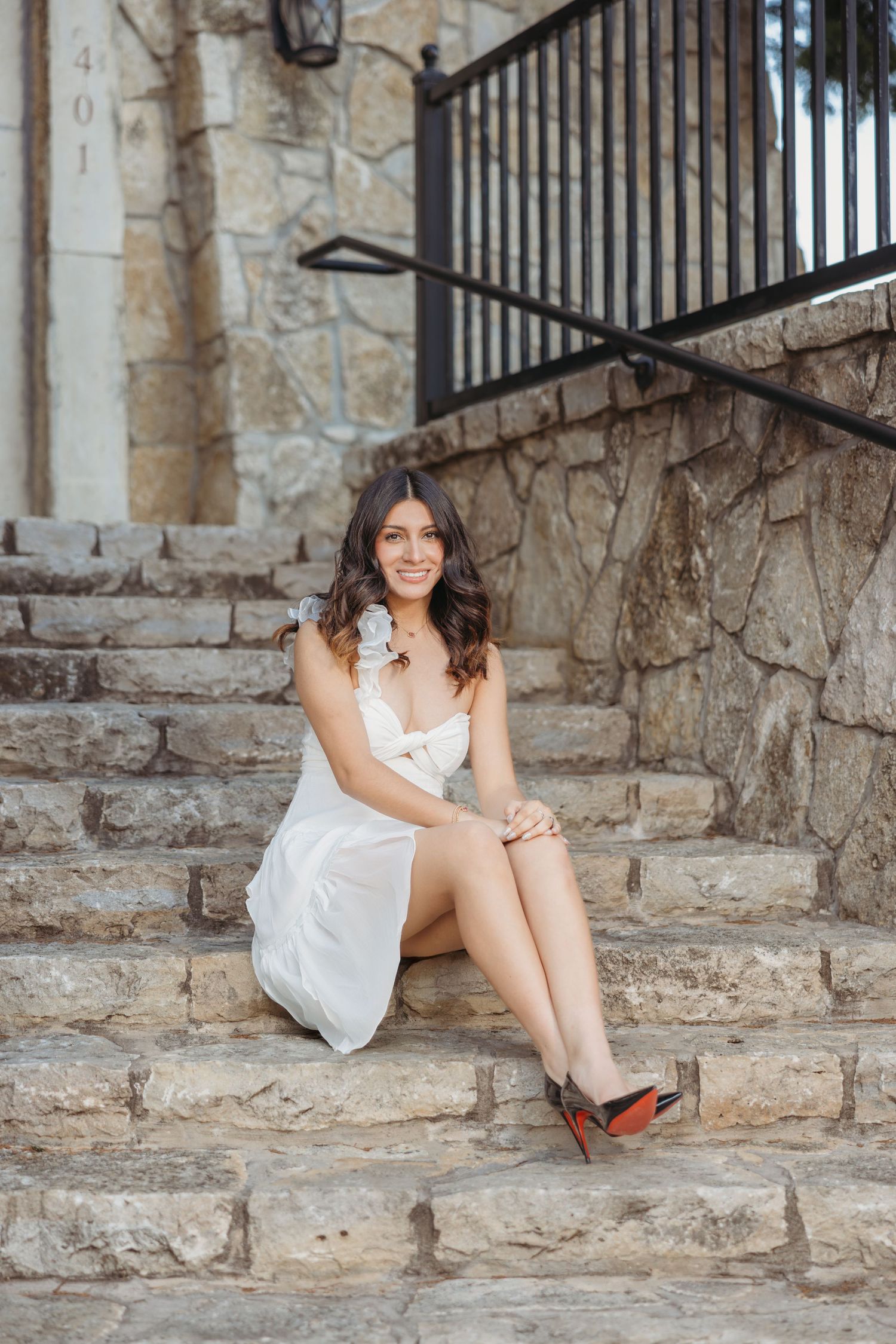 Young woman in white dress sitting on stone steps for senior portrait photography.
