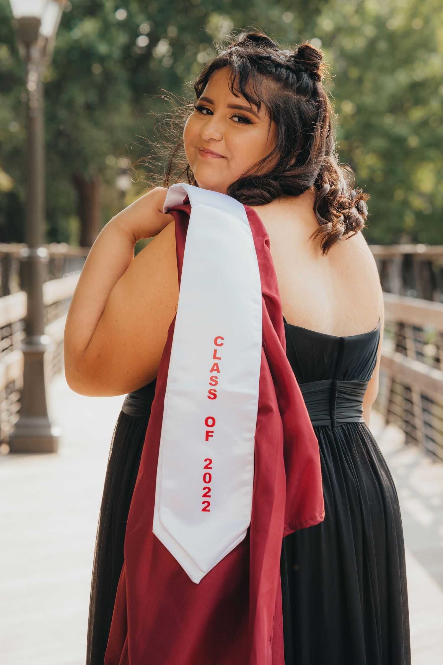 A young woman in a black gown displays her Class of 2022 graduation stole over her shoulder.