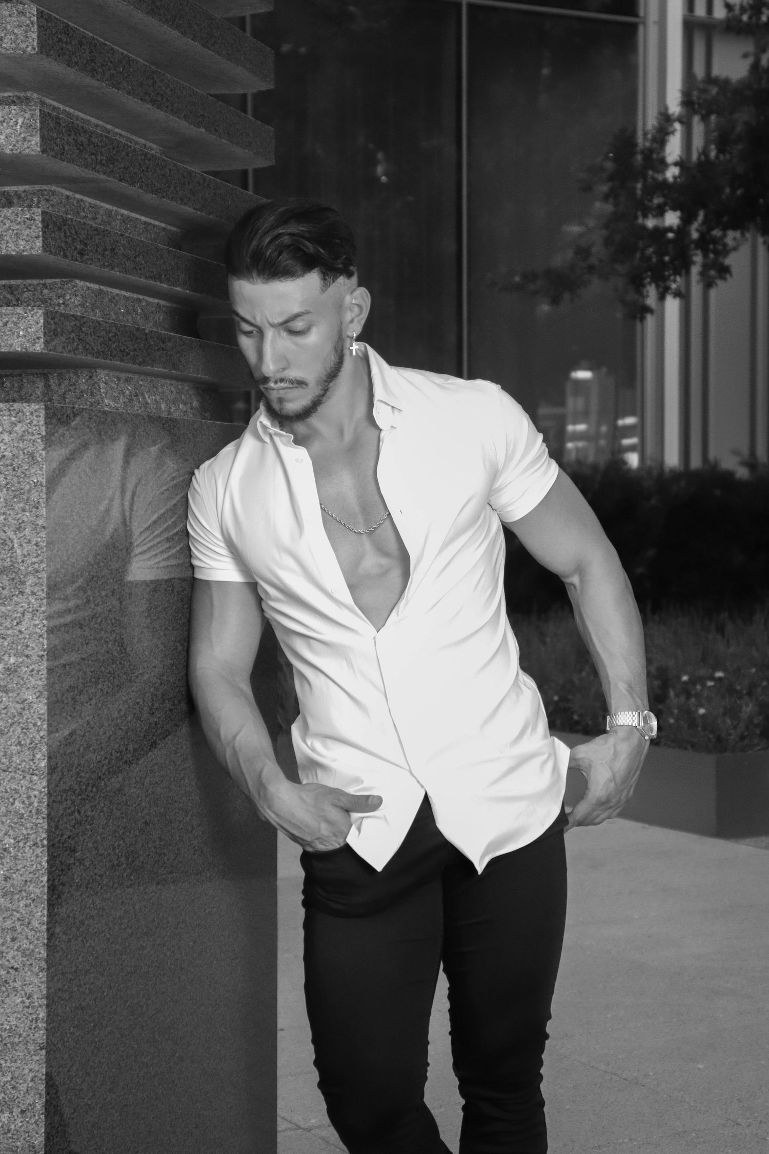 Athletic man in white shirt leaning against column in black and white urban photo.