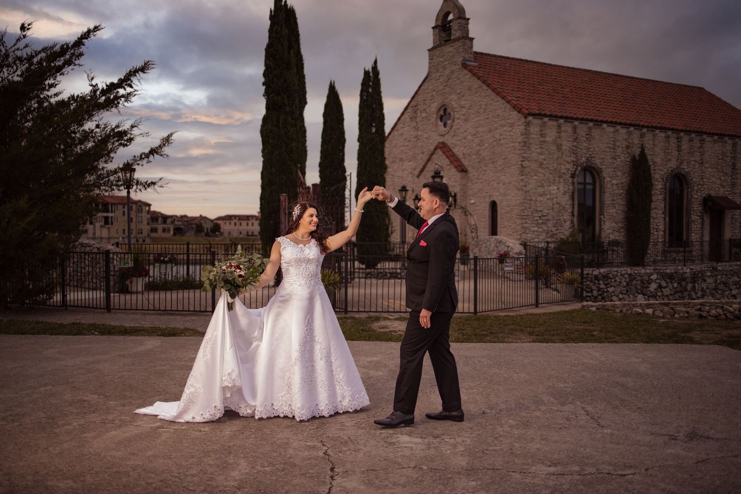 Bride and groom dancing outside historic stone church at sunset.
