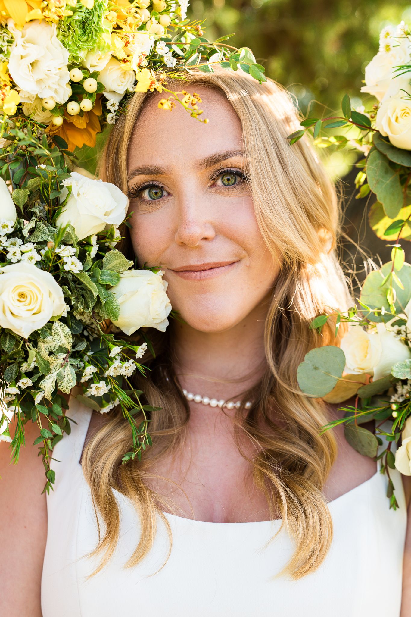 A floral crown with white roses and greenery adorns a bridal look with pearls and natural lighting.