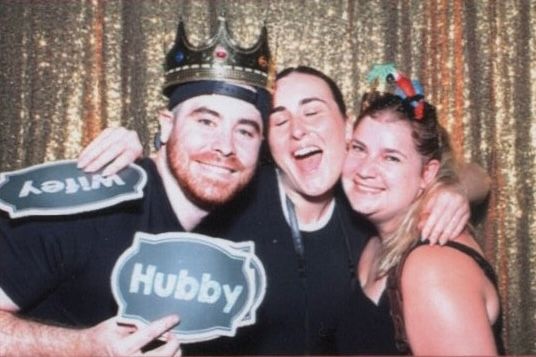 Group of friends posing together in front of a sparkly gold sequin backdrop at a celebration event.
