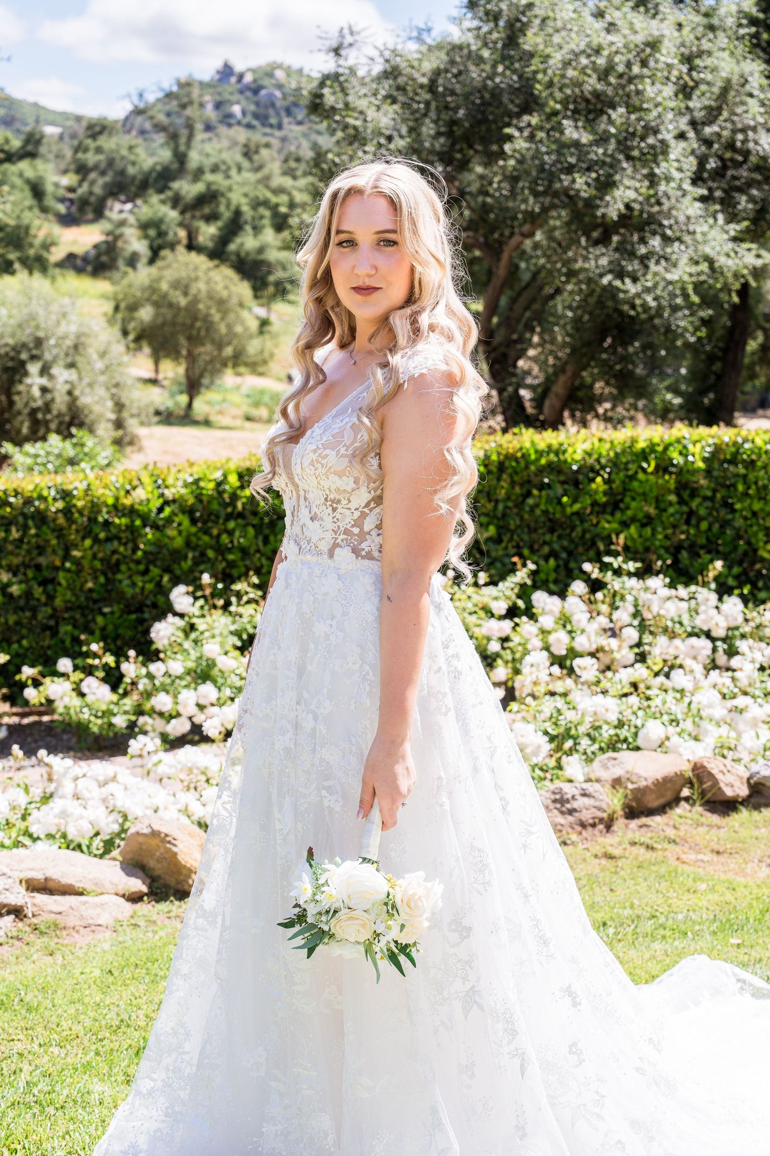 A wedding dress with delicate lace details and flowing tulle skirt in a sunny garden setting with white flowers.