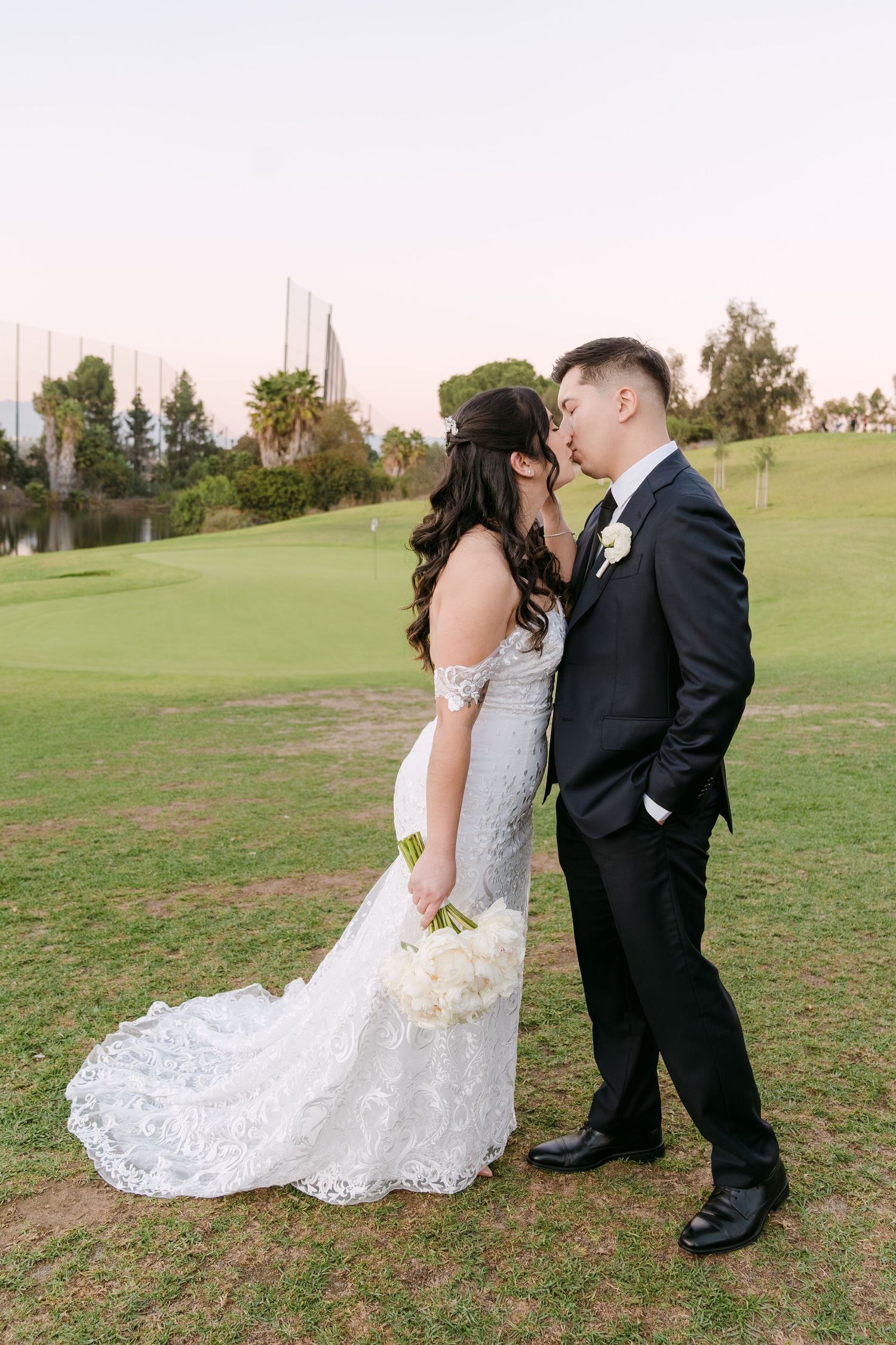 A couple in wedding attire shares an intimate moment on a grassy hill during golden hour.