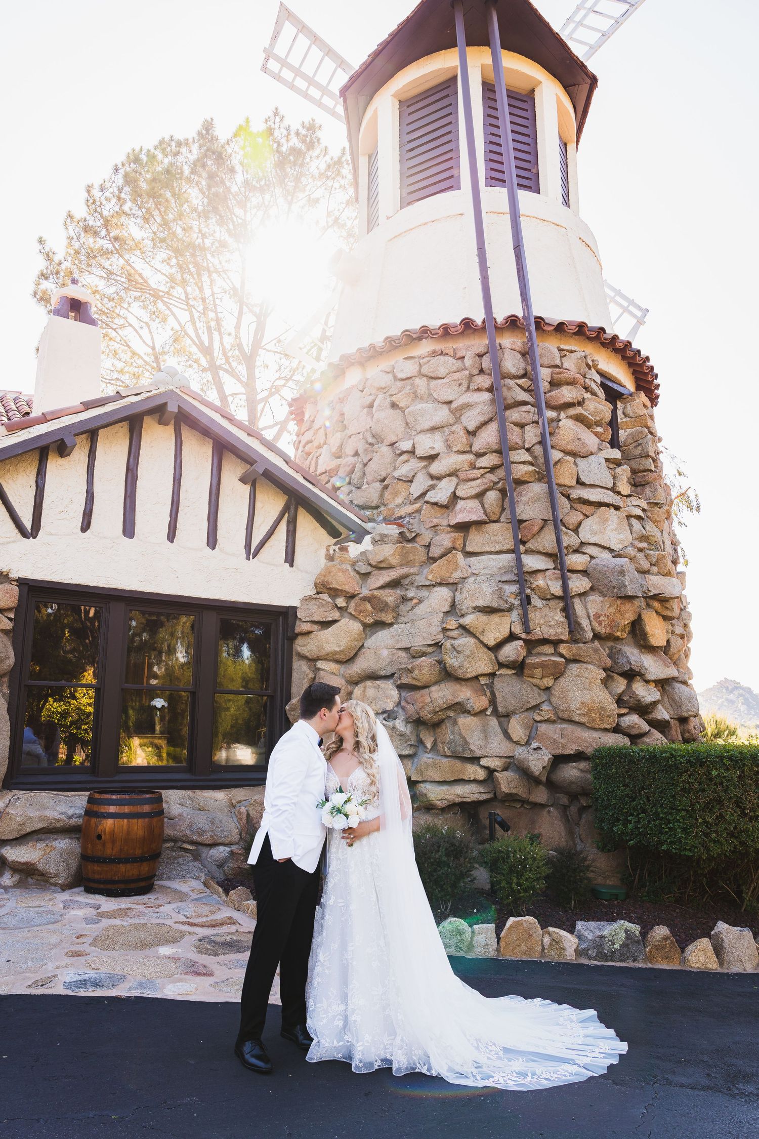 A romantic wedding couple poses against a rustic stone wall backdrop at a charming venue during sunset.