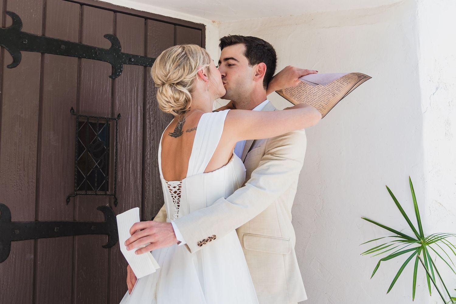 A bride and groom share a romantic kiss outside a rustic wooden door on their wedding day.