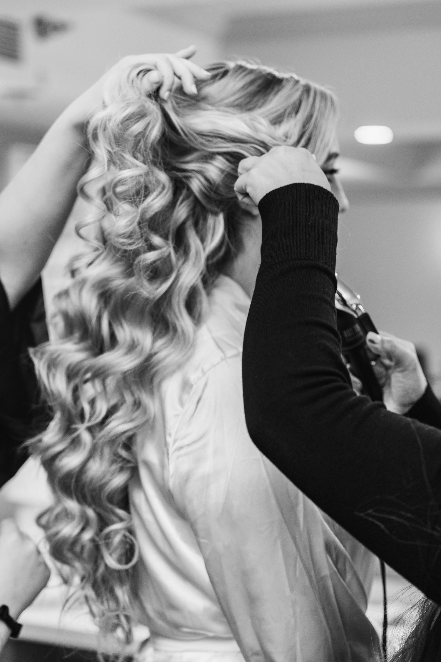 Black and white photo of a hairstylist styling long curly blonde hair for a wedding or formal event.