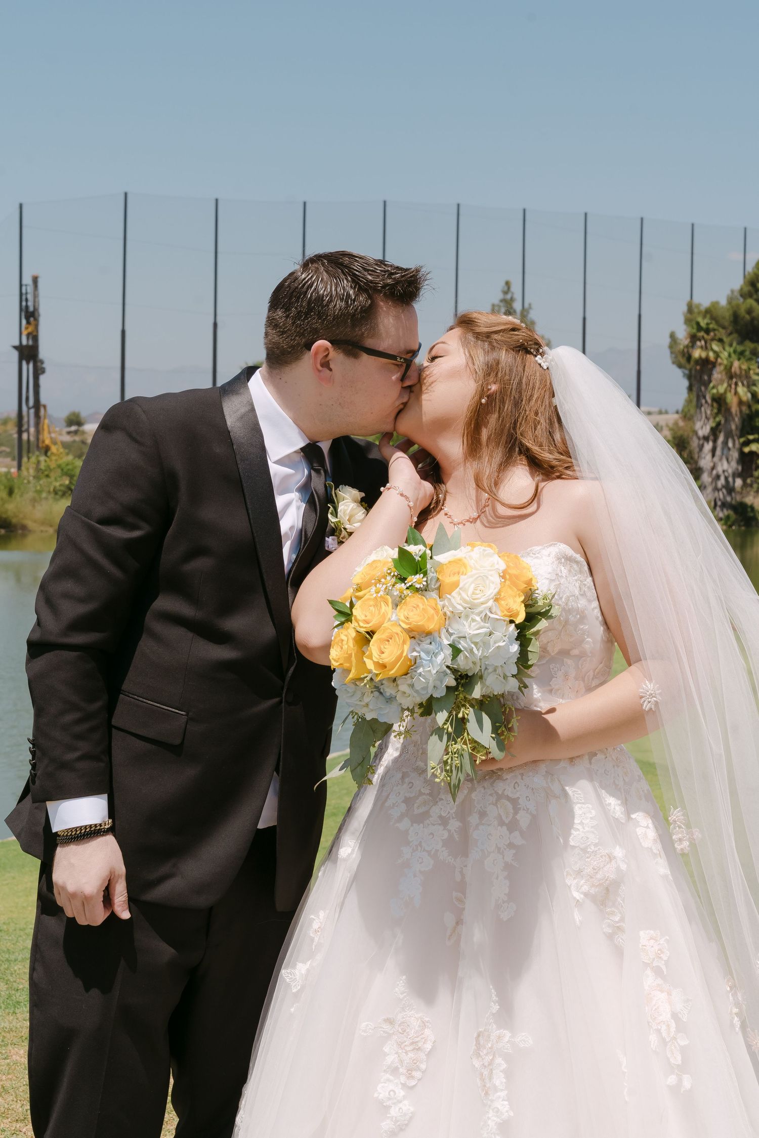 A romantic wedding sequence shows a couple sharing their first kiss as newlyweds outdoors on a sunny day.
