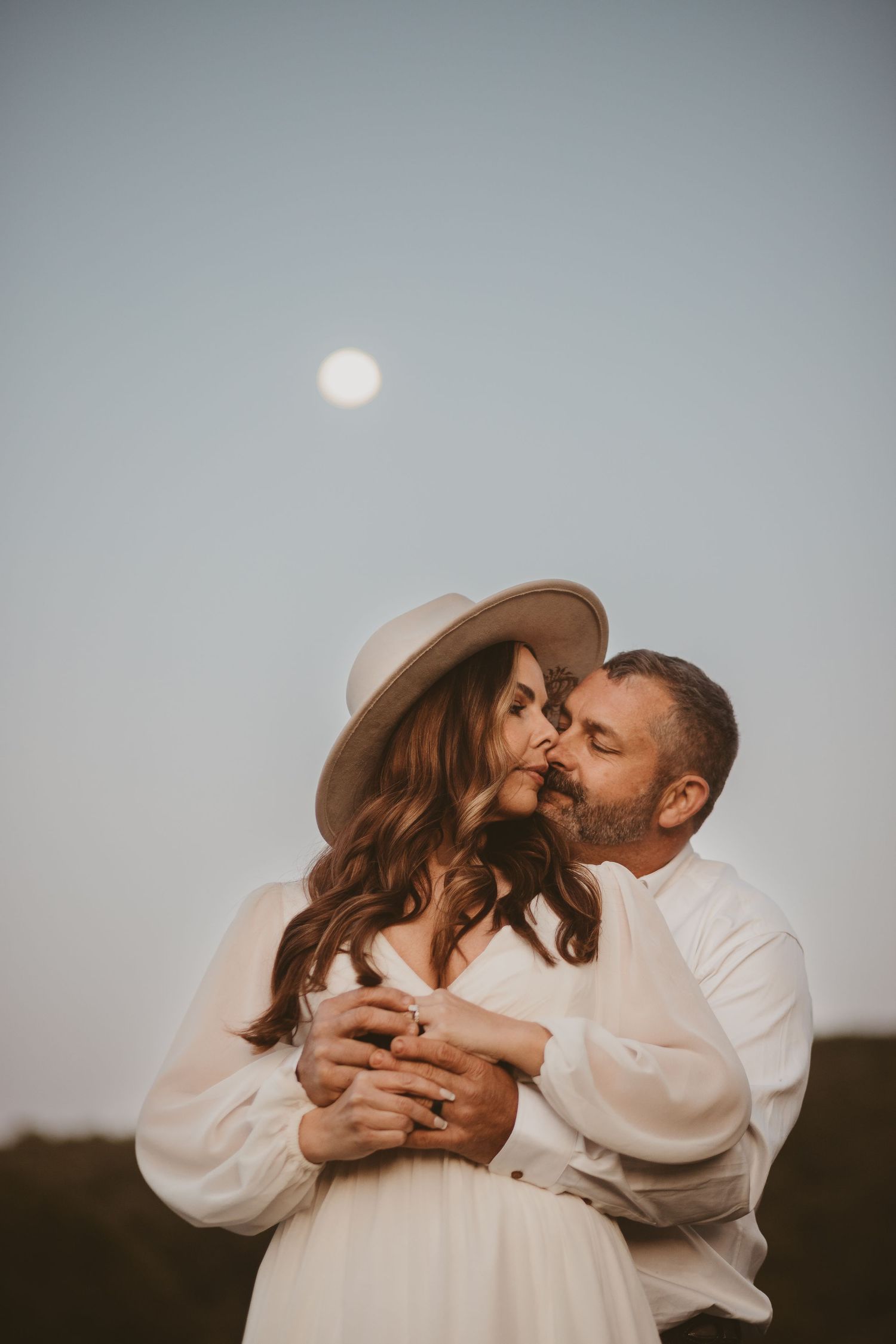 Intimate couple portrait with soft lighting against a dreamy sky backdrop.