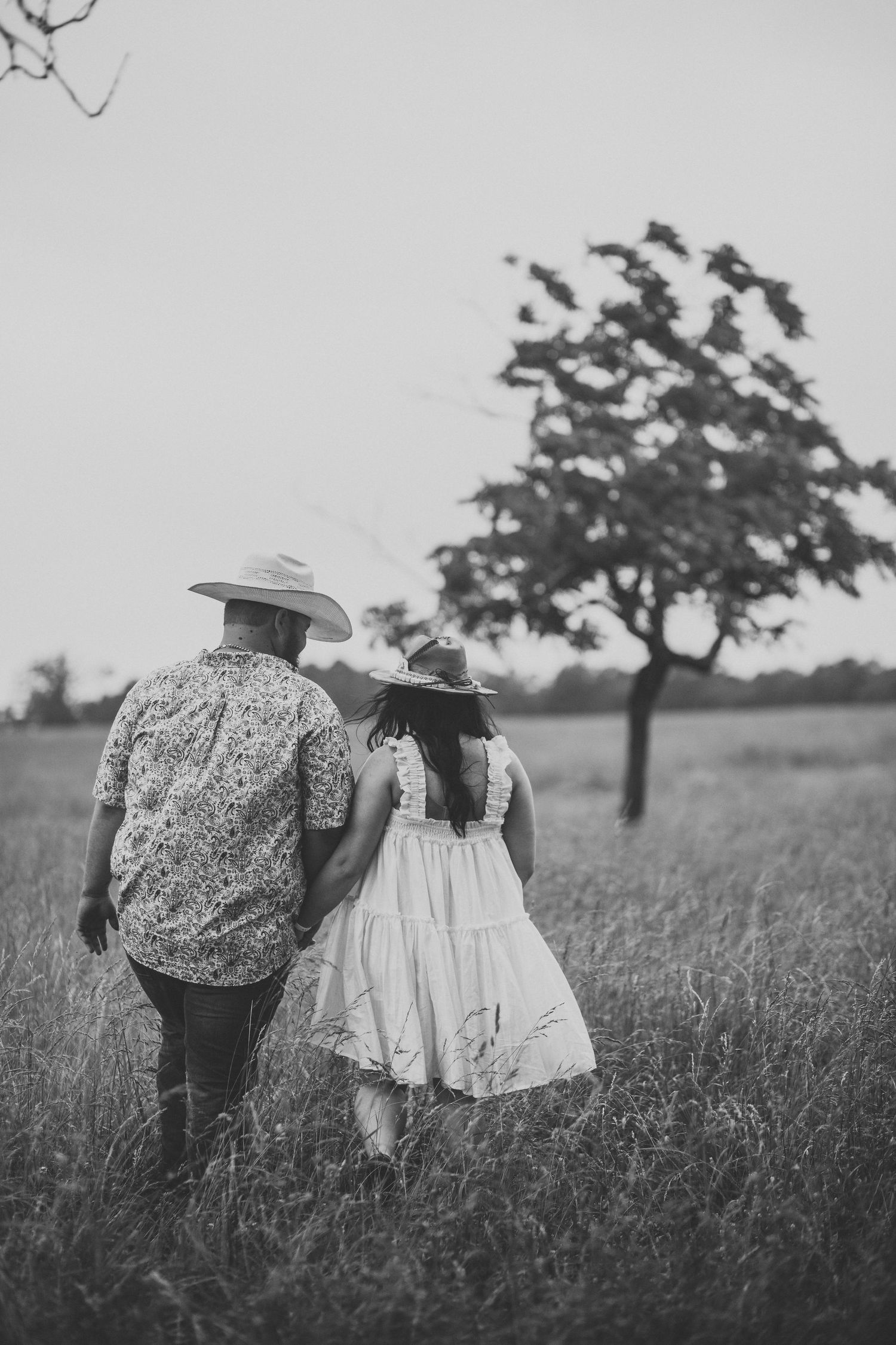 Two people in vintage clothing walk through tall grass field at sunset.