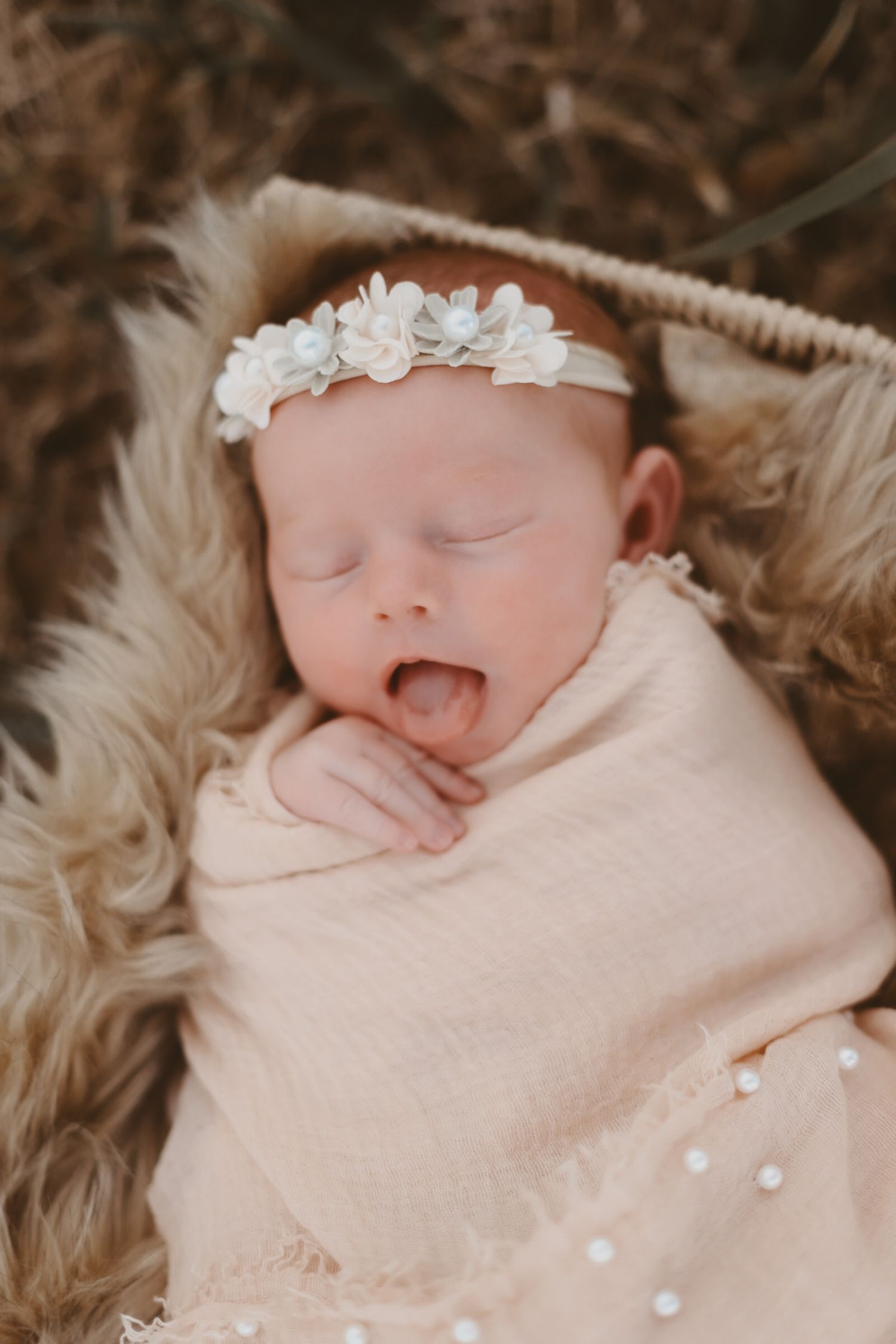Sleeping newborn wrapped in pink blanket wearing delicate floral headband.