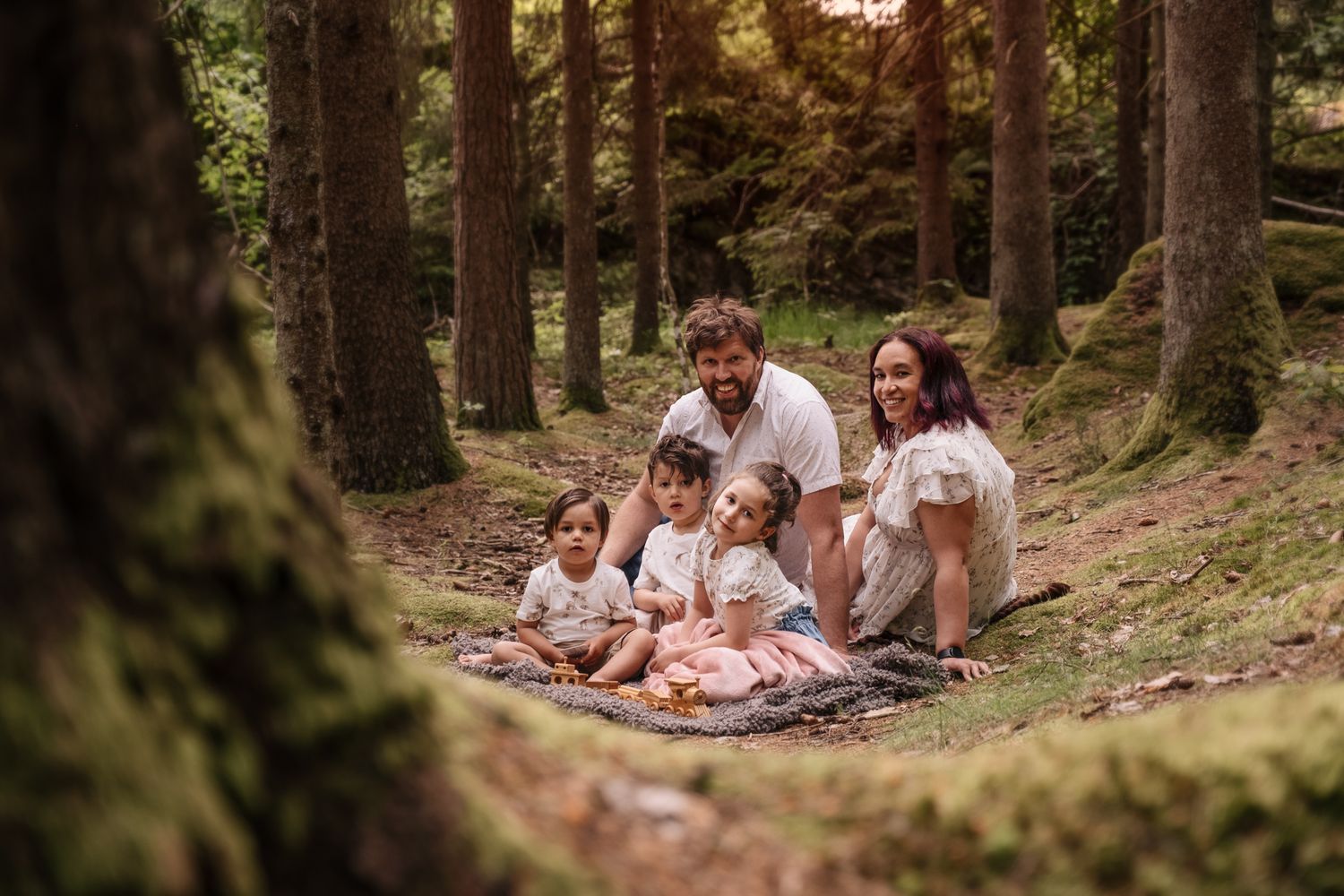 En familj sitter tillsammans i en skogsglänta och har det mysigt tillsammans