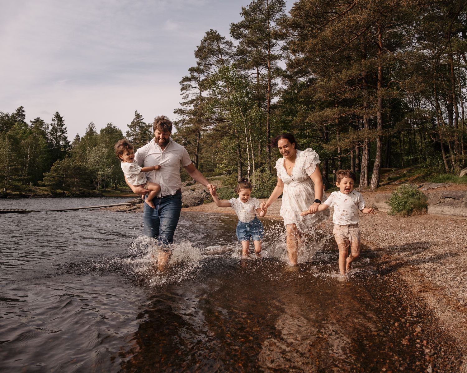 Lekfull familjebild där familjen springer i vattenbrynet tillsammans