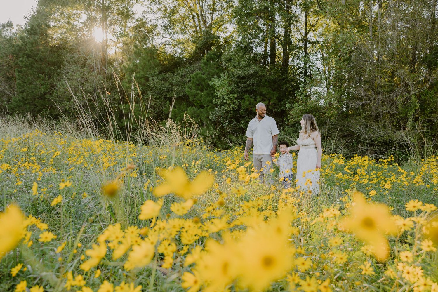 Two people walk together through a vibrant meadow of yellow wildflowers at sunset with trees in the background.