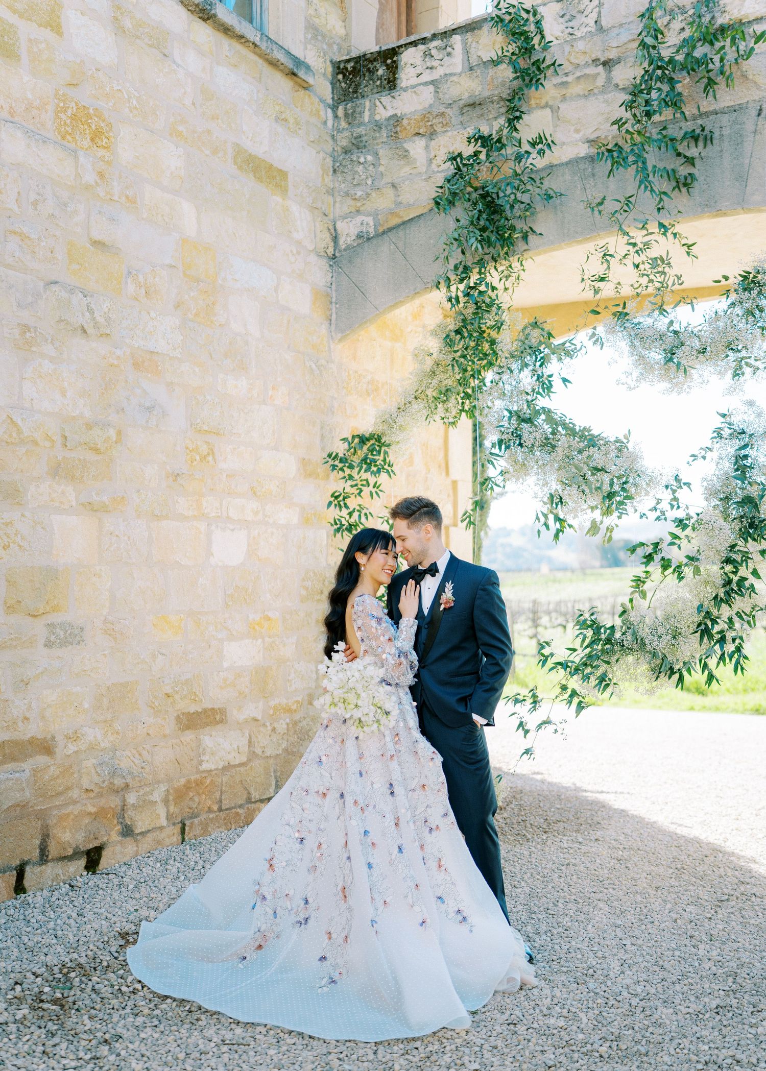 A bride and groom share romantic moments in a stone archway covered with cascading greenery during their wedding photoshoot.