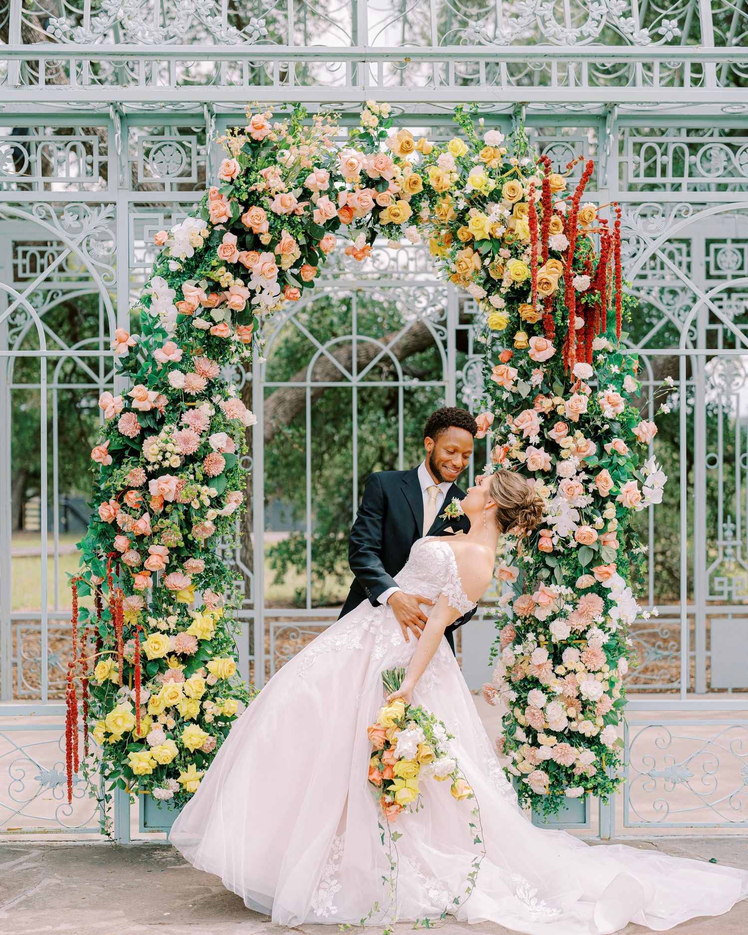 Romantic wedding photoshoot in an ornate white gazebo decorated with cascading peach and yellow roses and floral arrangements.