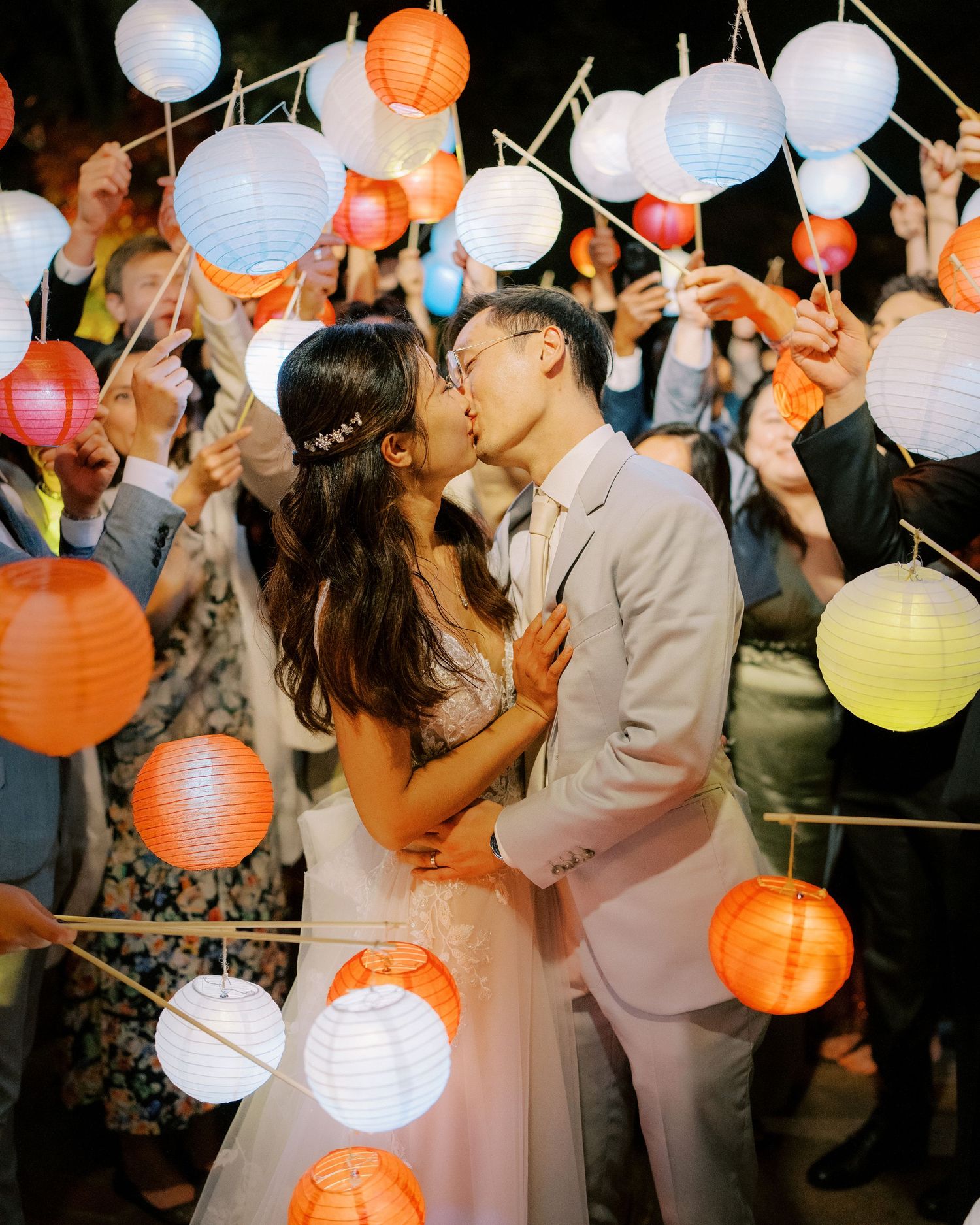 Wedding celebration with colorful paper lanterns in orange, white and blue illuminating a lively dance floor.