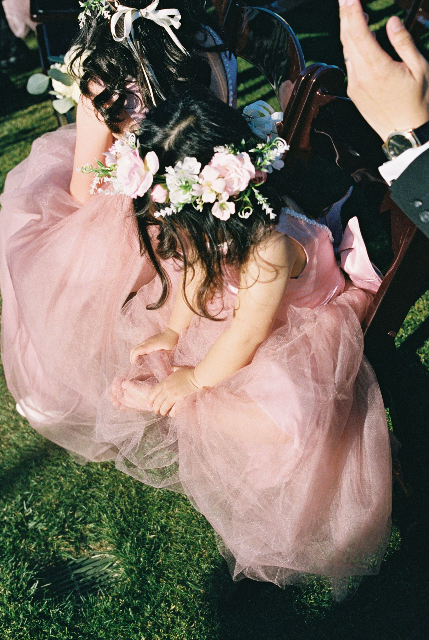A person in a pink tulle dress sits gracefully in a garden setting with delicate floral hair accessories.