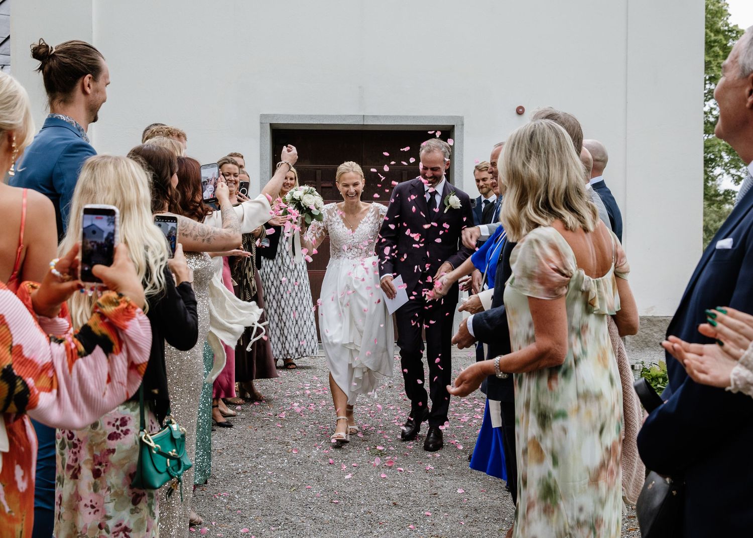 Newlyweds walking through confetti shower as wedding guests celebrate outside white church entrance.