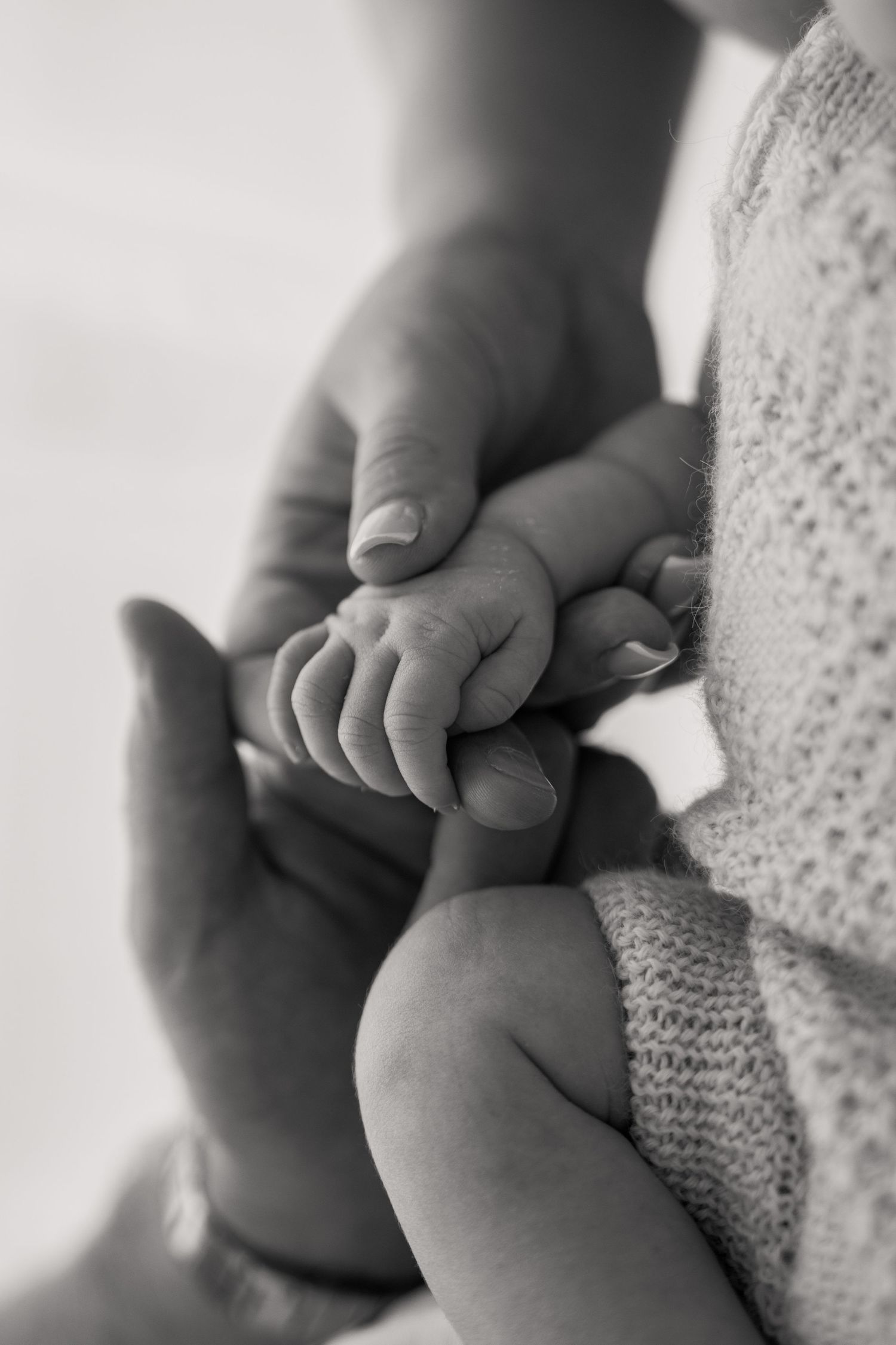 Black and white photo of a newborn baby's tiny hand grasping an adult's finger, symbolizing love and new life.