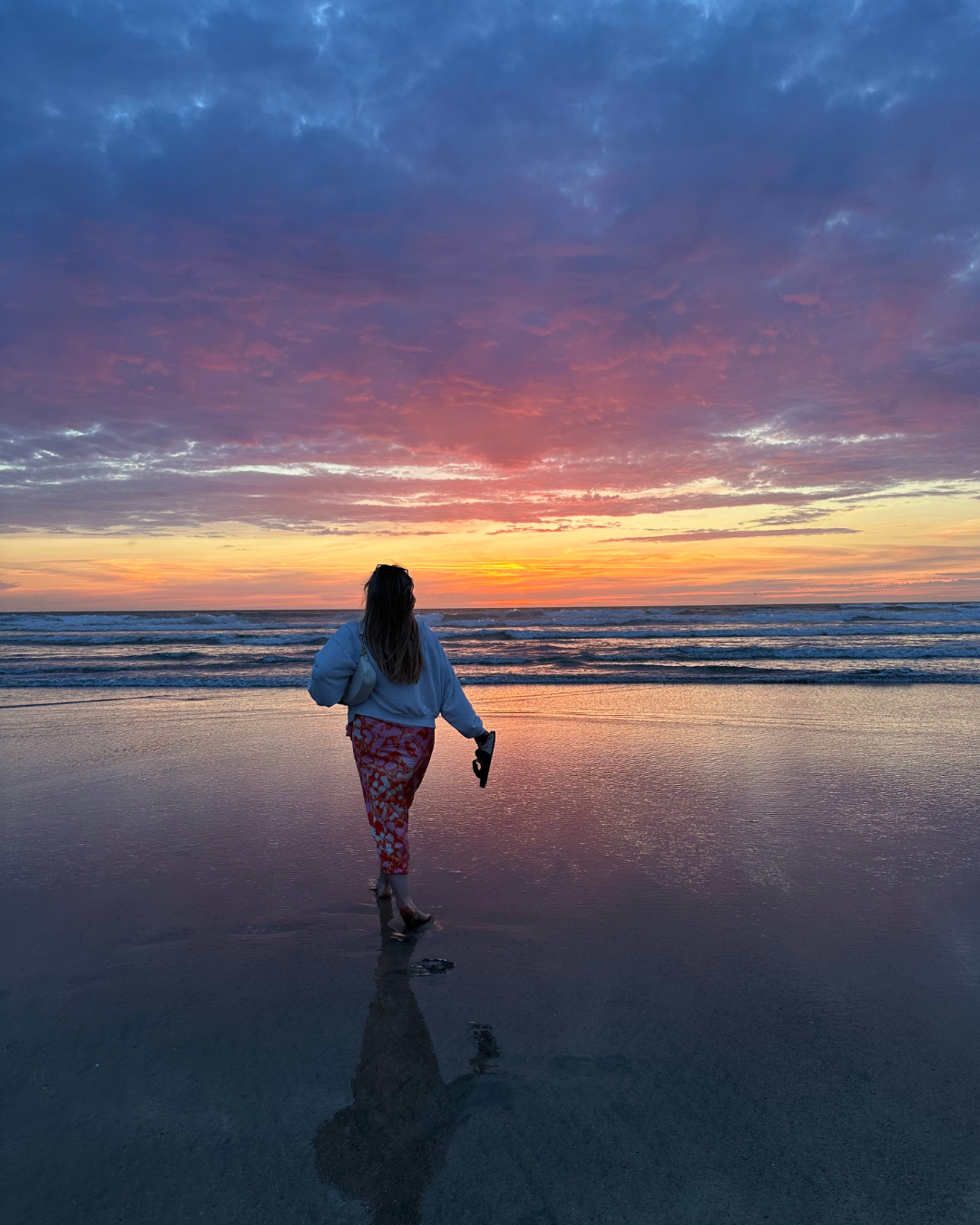 A silhouette runs along a sandy beach at sunset with vibrant orange and purple clouds reflecting on the water.