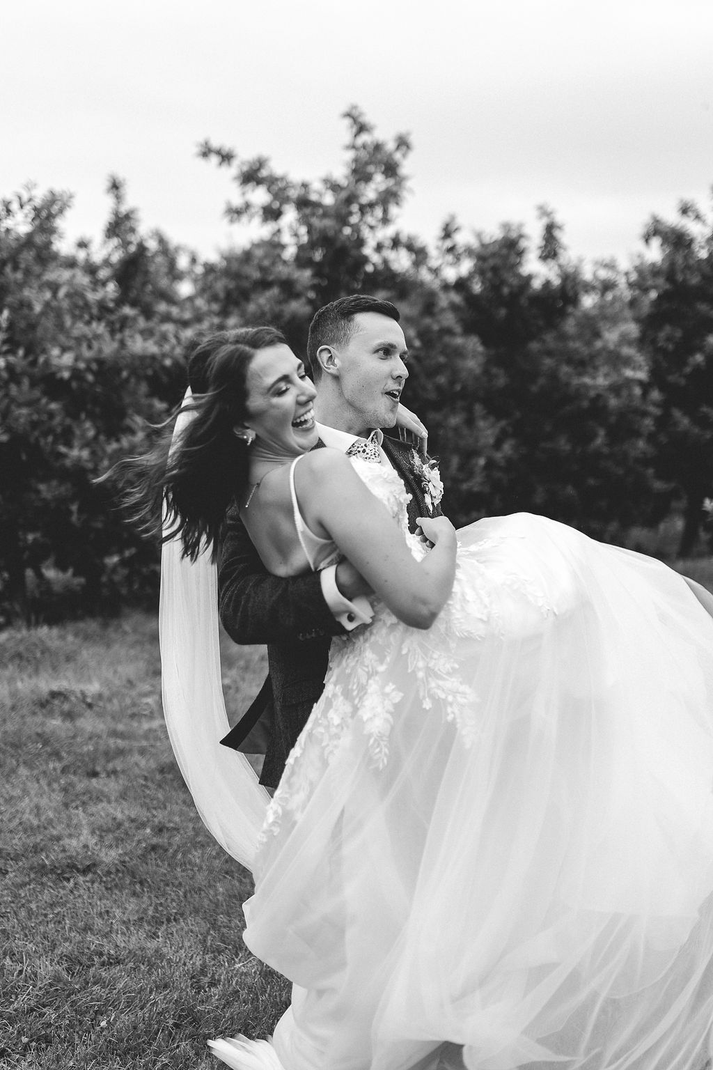 A playful wedding moment captured in black and white as a couple dances and laughs together outdoors.