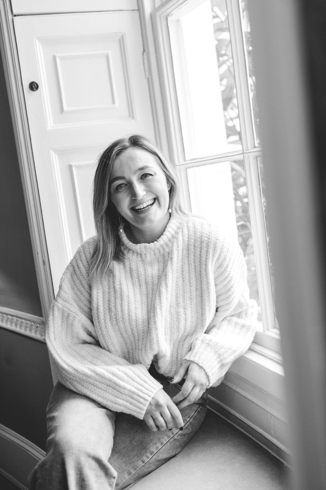 A person in a white turtleneck sweater sits by a window in a series of black and white photos showing different poses.