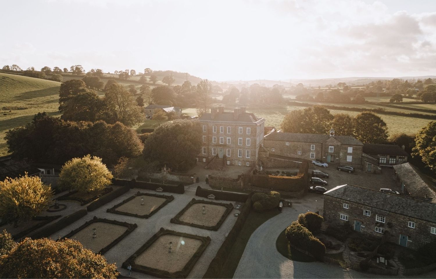 Aerial panoramic view of a historic castle estate with manicured gardens during golden sunset.