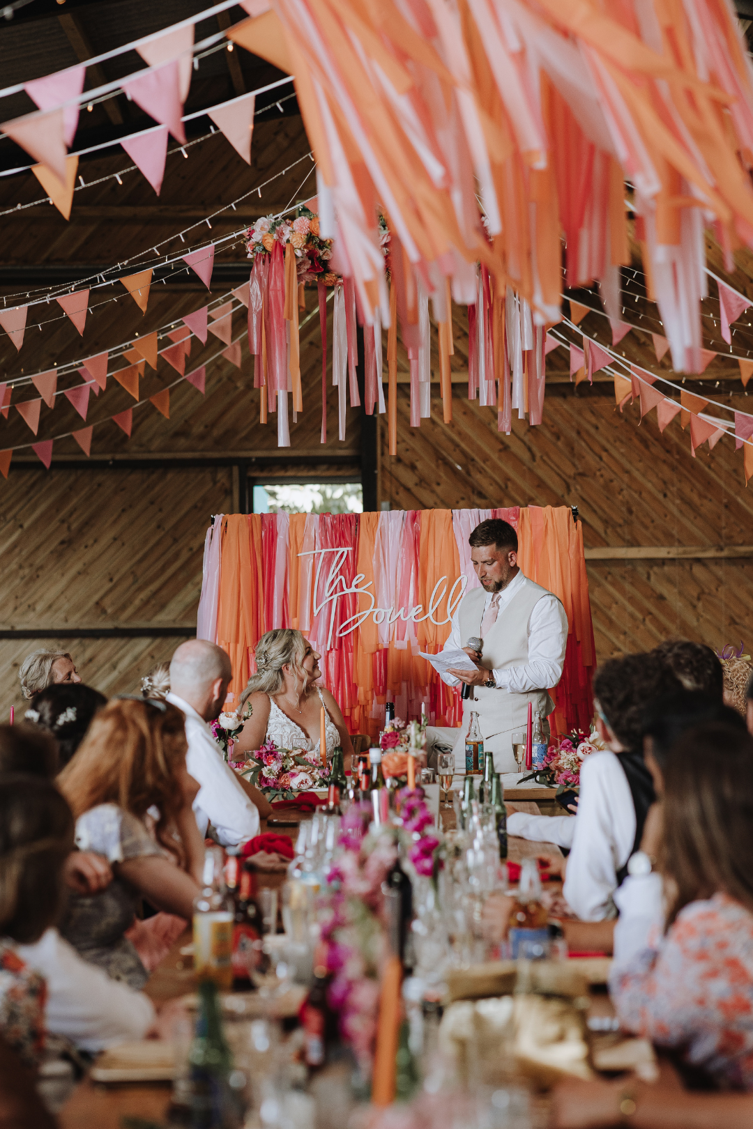 Wedding reception table setup in rustic barn venue with pink streamers and bunting decorations overhead.