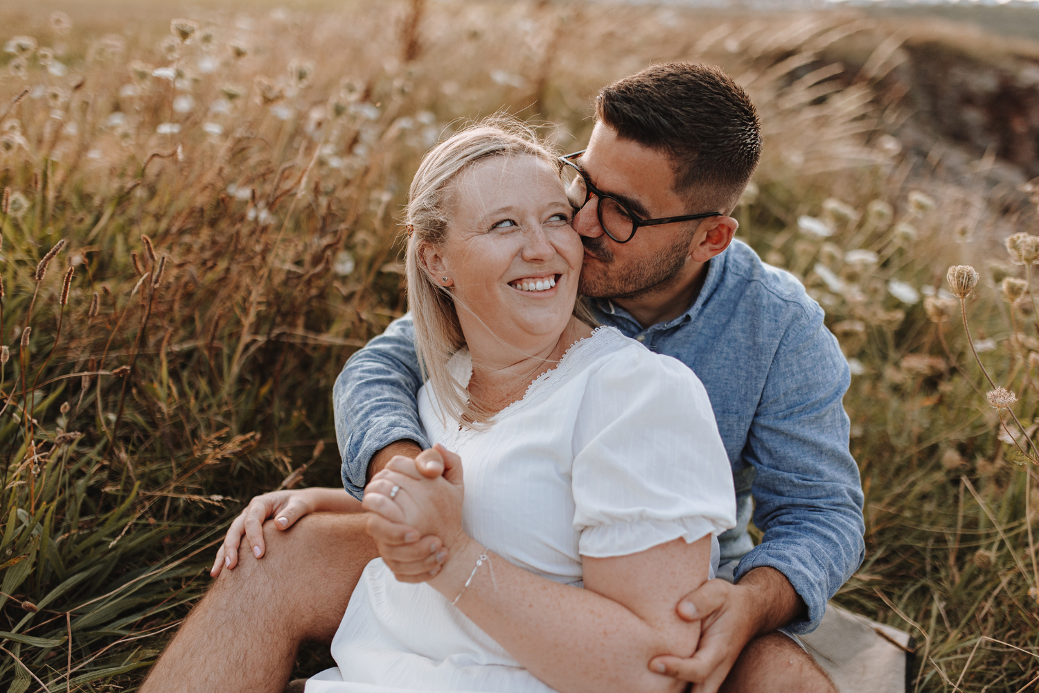 Romantic couple embraces in golden field of wildflowers during sunset photoshoot.