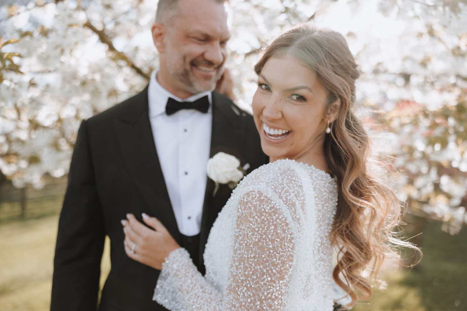 A wedding couple sharing romantic moments surrounded by blooming cherry blossoms on a beautiful spring day.