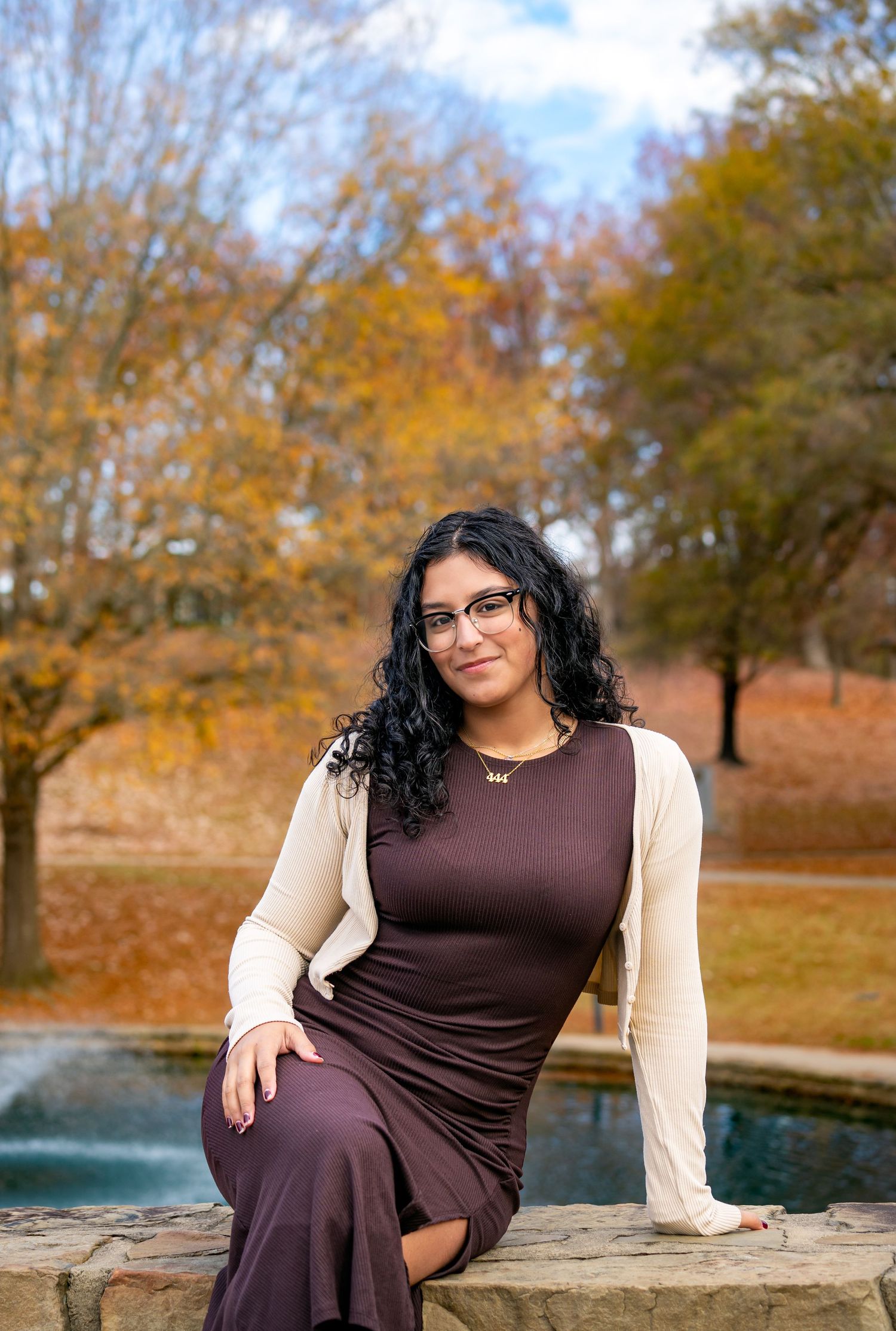 Autumn maternity photoshoot by a pond with fall foliage in the background.