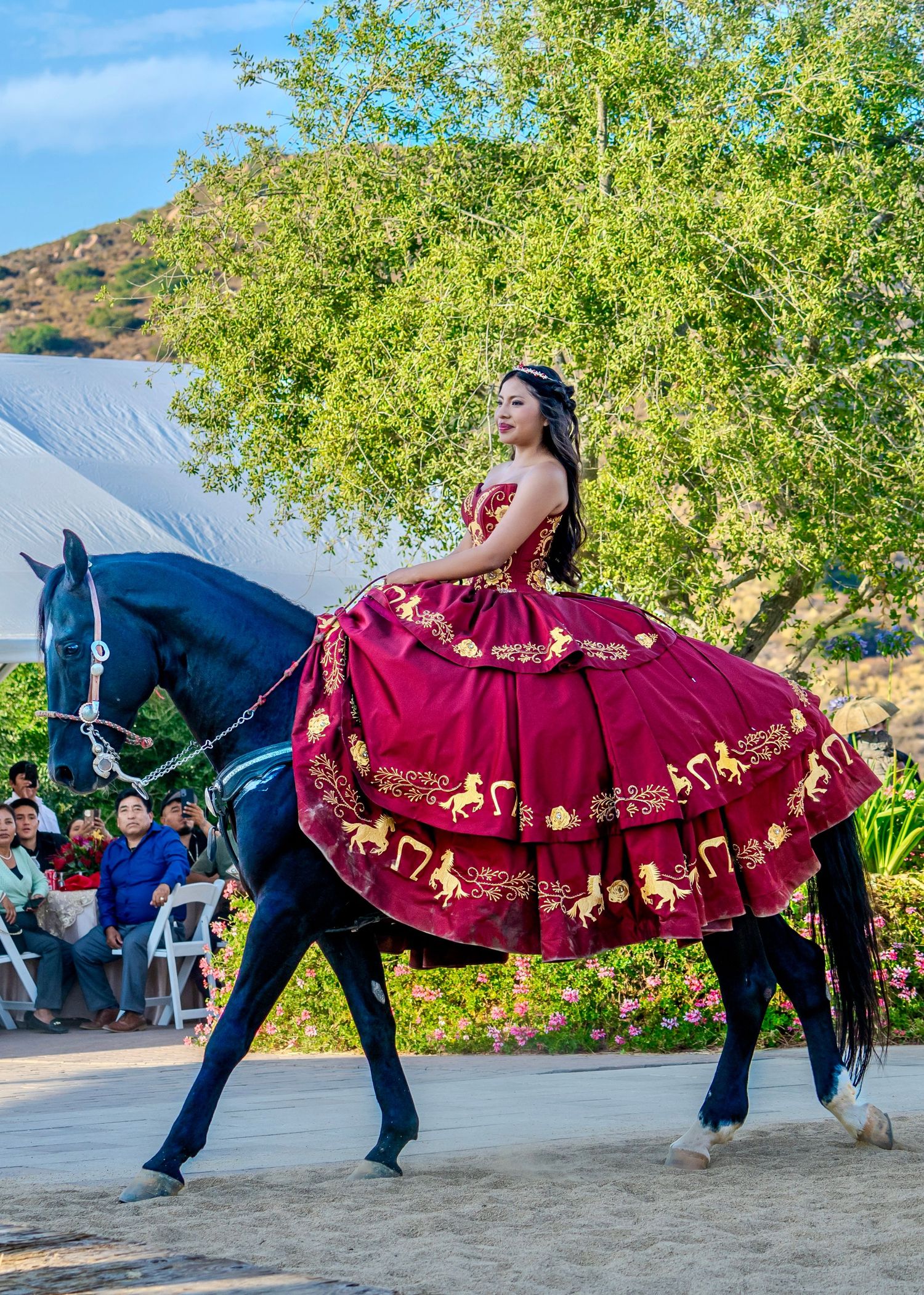 A red and gold embellished dress displayed while riding horseback under green trees.