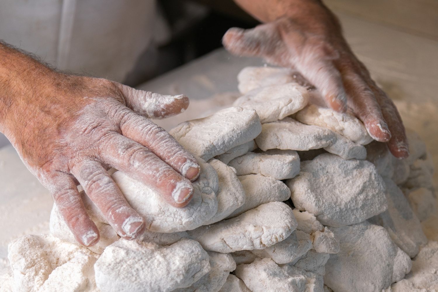 Hands kneading and shaping raw dough on a floured surface in a sequence of preparation steps.