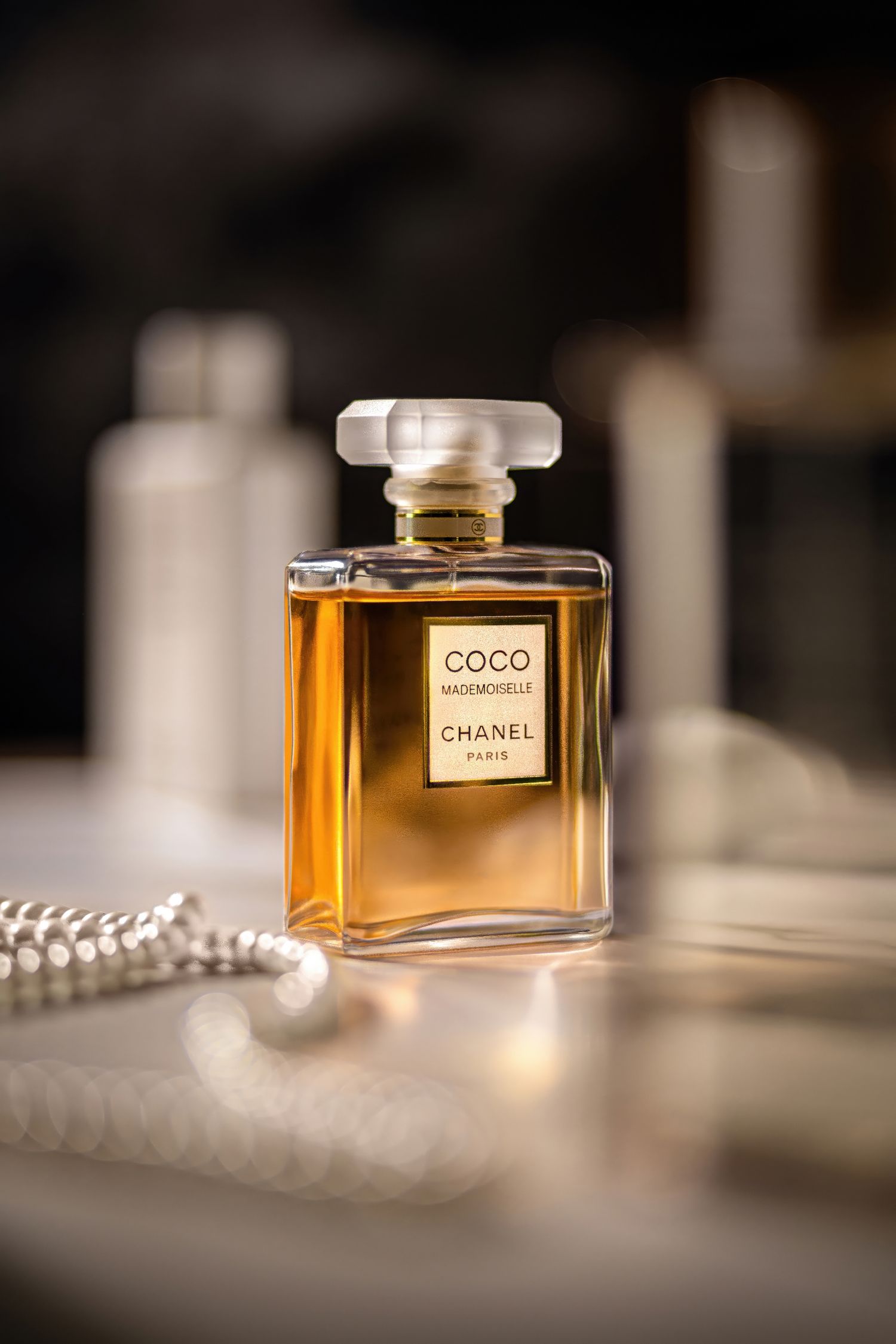 Elegant Chanel Coco perfume bottle with pearl necklace in soft focus lighting creating a luxurious product shot.