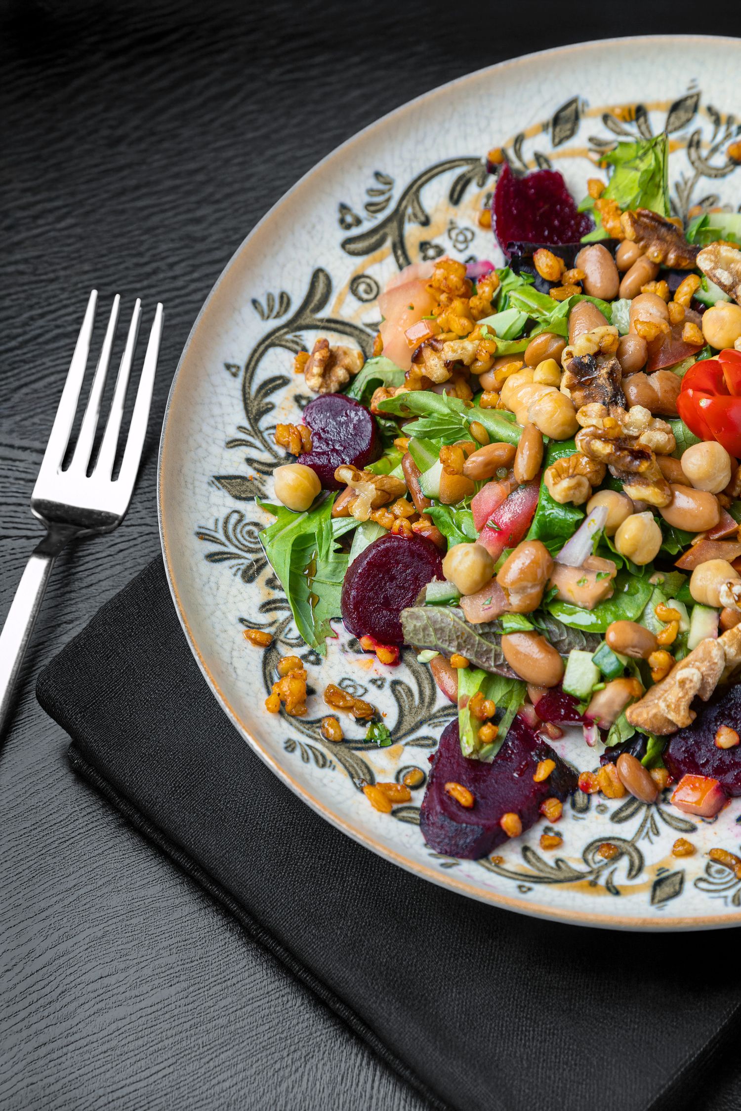 A vibrant chickpea salad with roasted beets, tomatoes and fresh herbs served on a decorative plate with a black fork.
