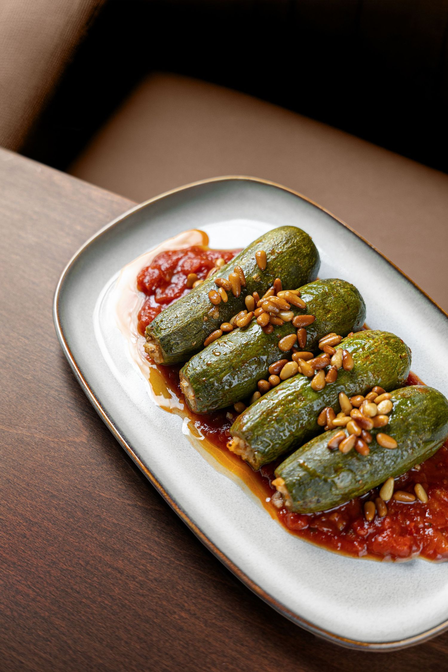 Stuffed grape leaves dolma served on tomato sauce, topped with toasted pine nuts on a white ceramic plate.