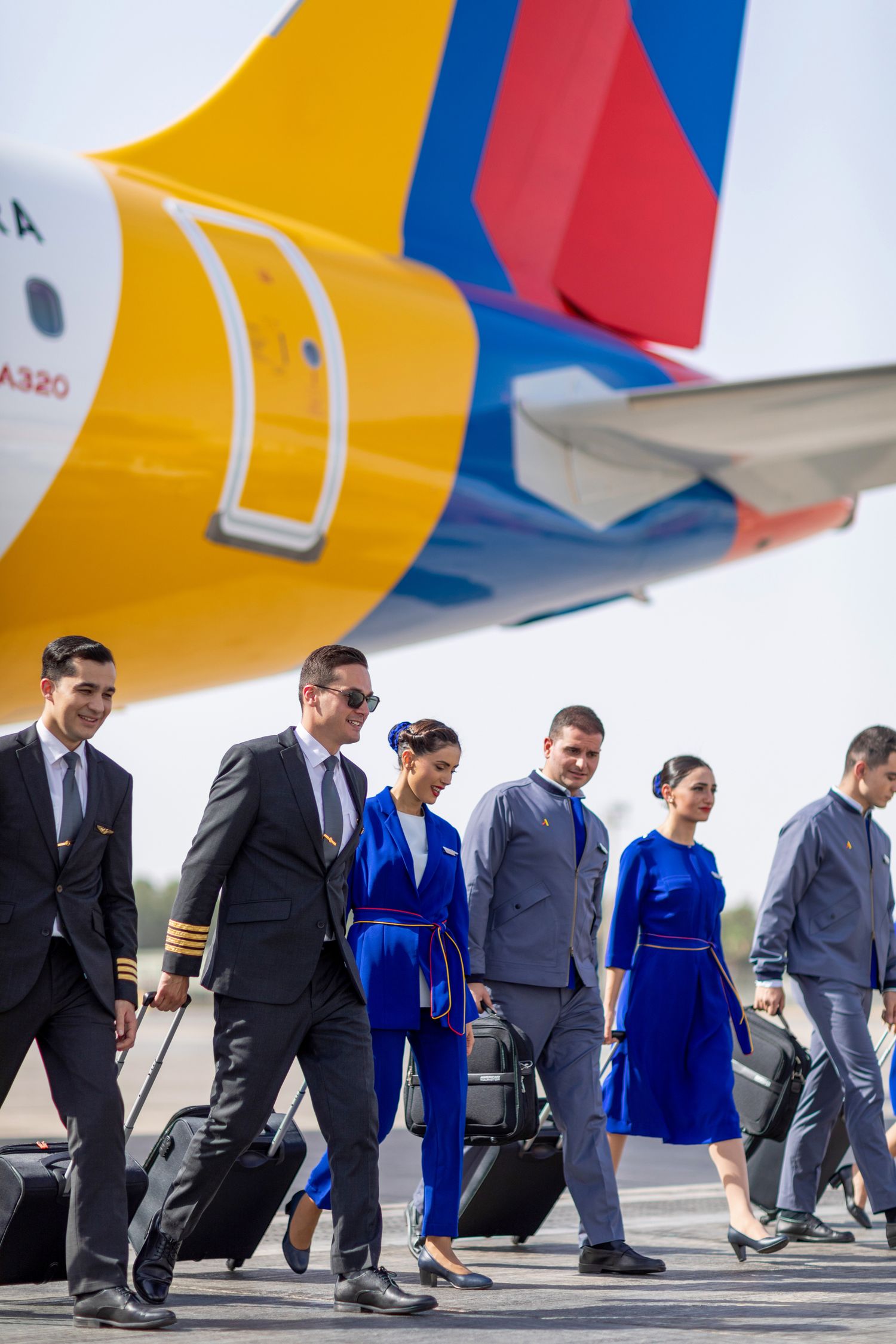 Airline ground crew walking on the runway near a multicolor aircraft tail, captured for branded airline photography and corporate video.