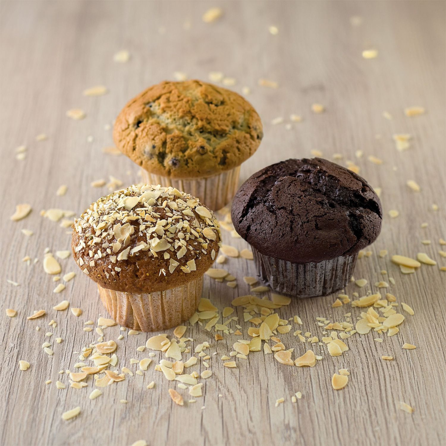 Assorted muffins and cupcakes photography with oats scattered on rustic wooden surface in warm lighting.