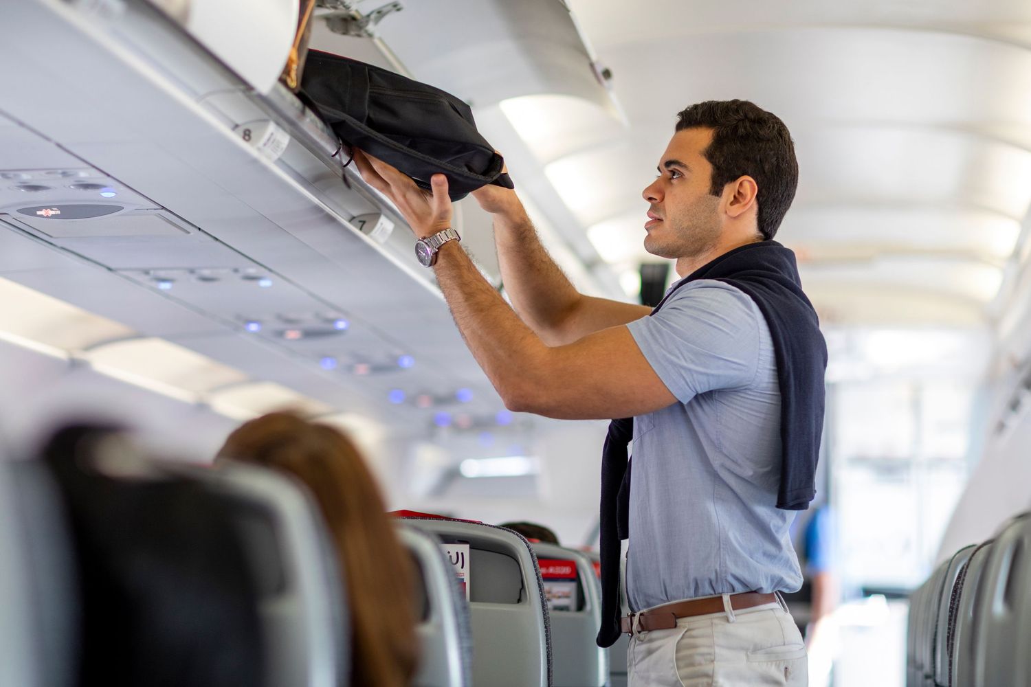 Airline passenger places a bag in the overhead bin during an in-cabin commercial shoot for branded airline visual content.