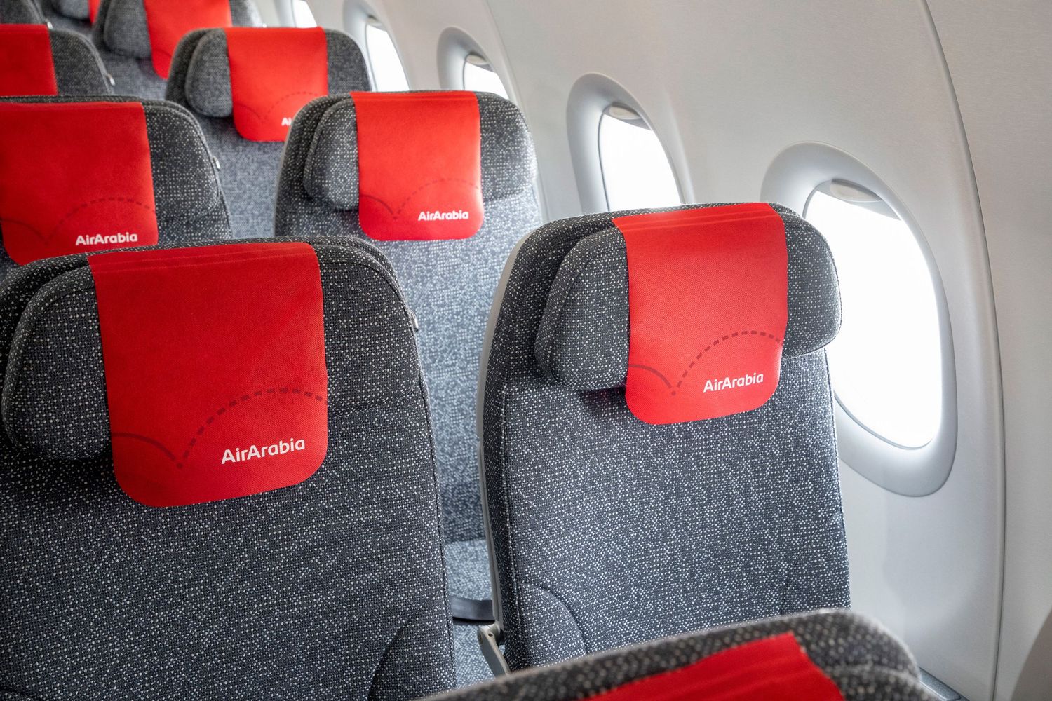 Interior of a modern aircraft with red headrest seats and wide passenger spaces, captured for corporate content.
