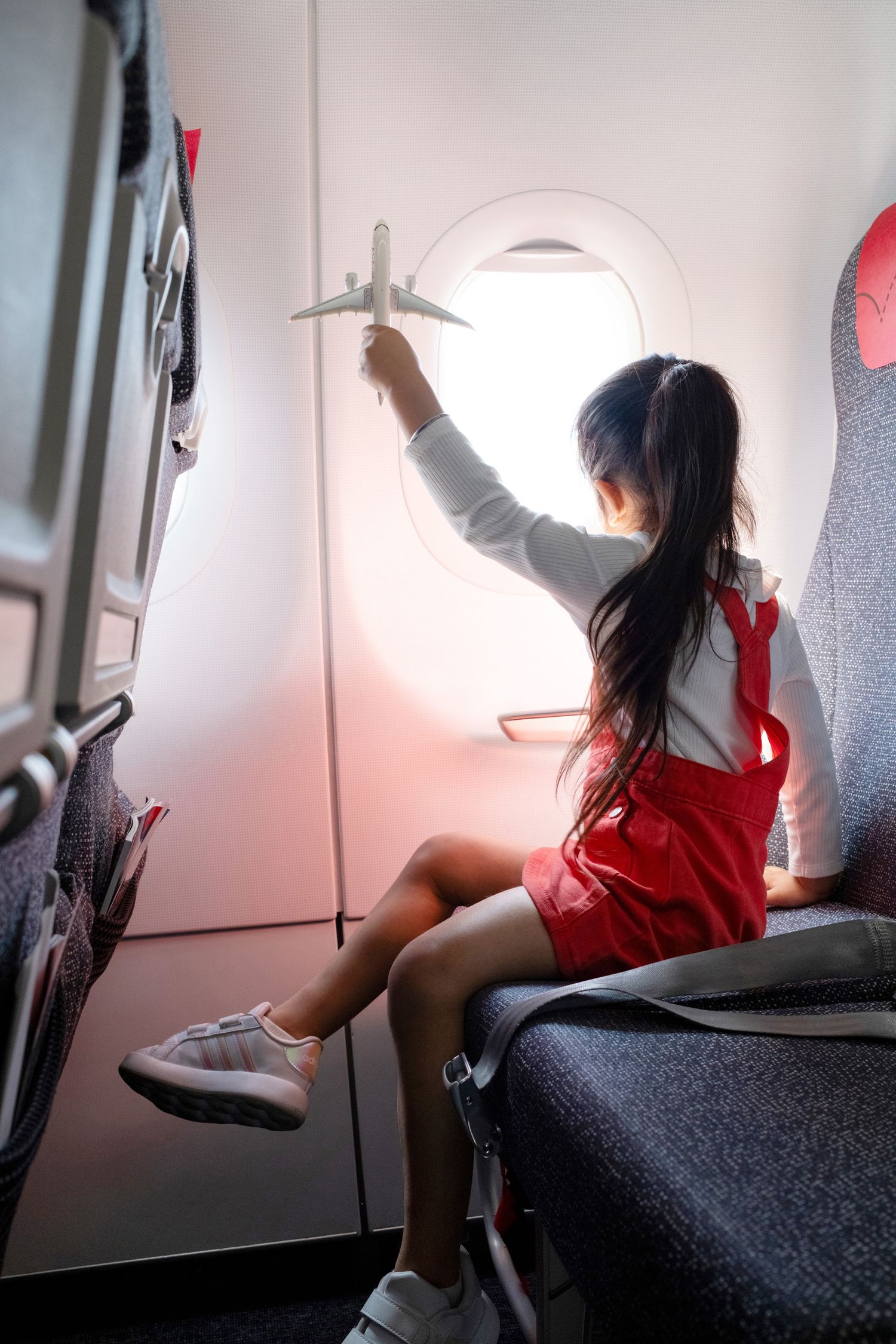 Child seated by airplane window gazing outside mid-flight – in-cabin aviation lifestyle photography