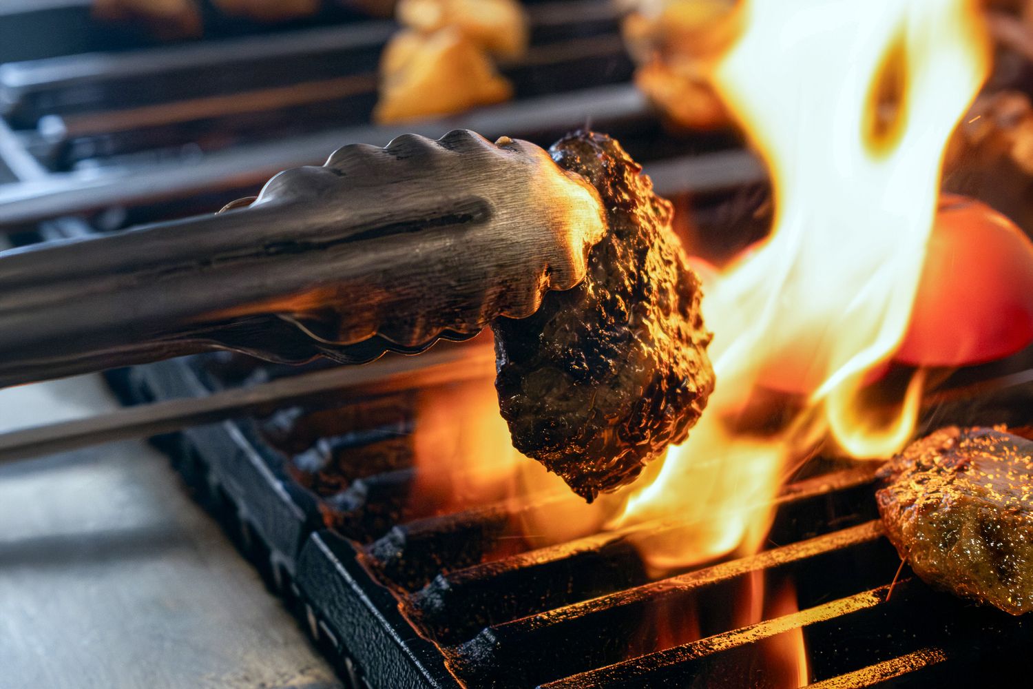 Flames engulf a juicy burger patty on a hot barbecue grill with metal grates.